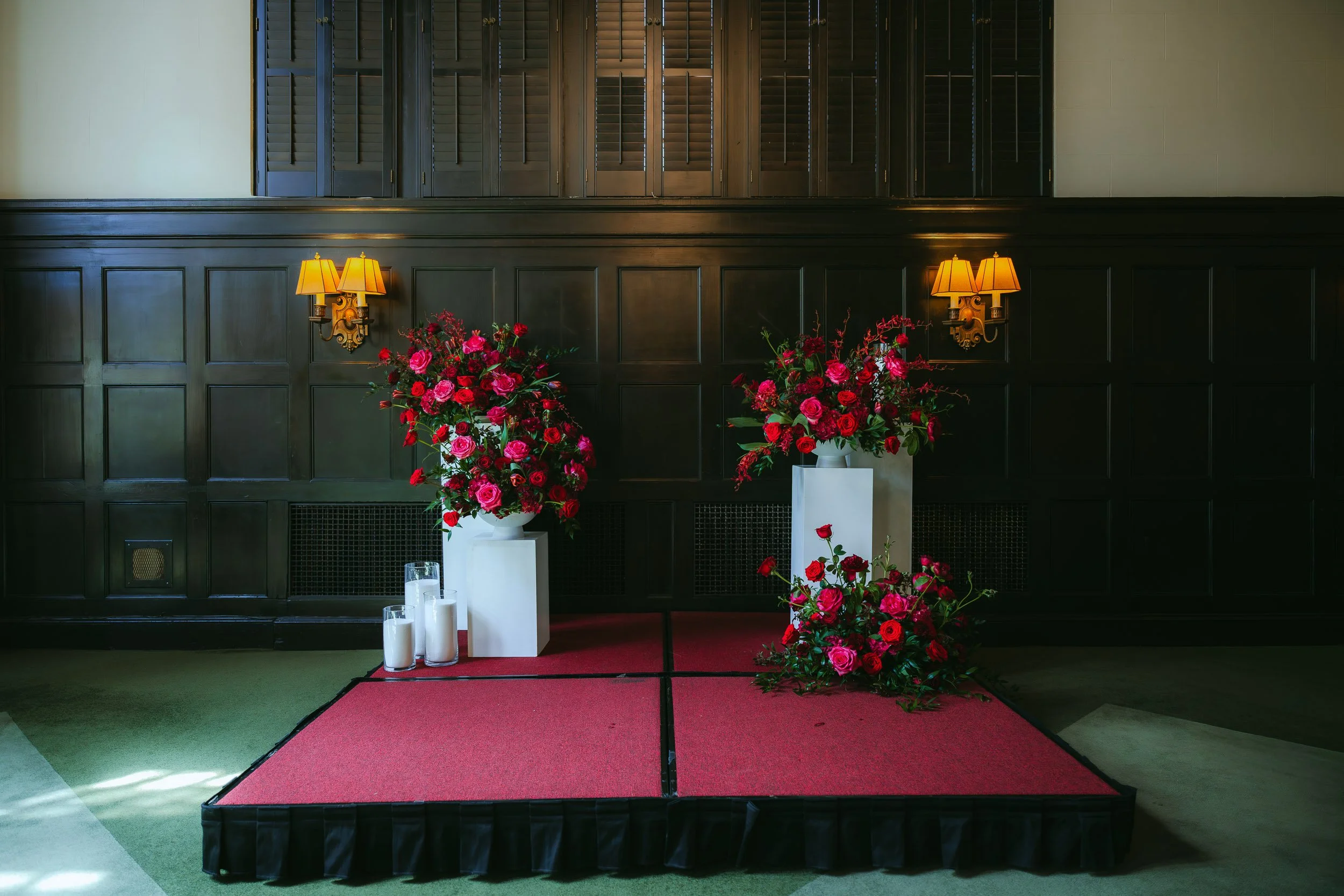 Jewel tone floral ceremony arrangements inside the University Club of Portland ballroom with romantic red and pink flowers, candles, and elegant wedding ceremony styling