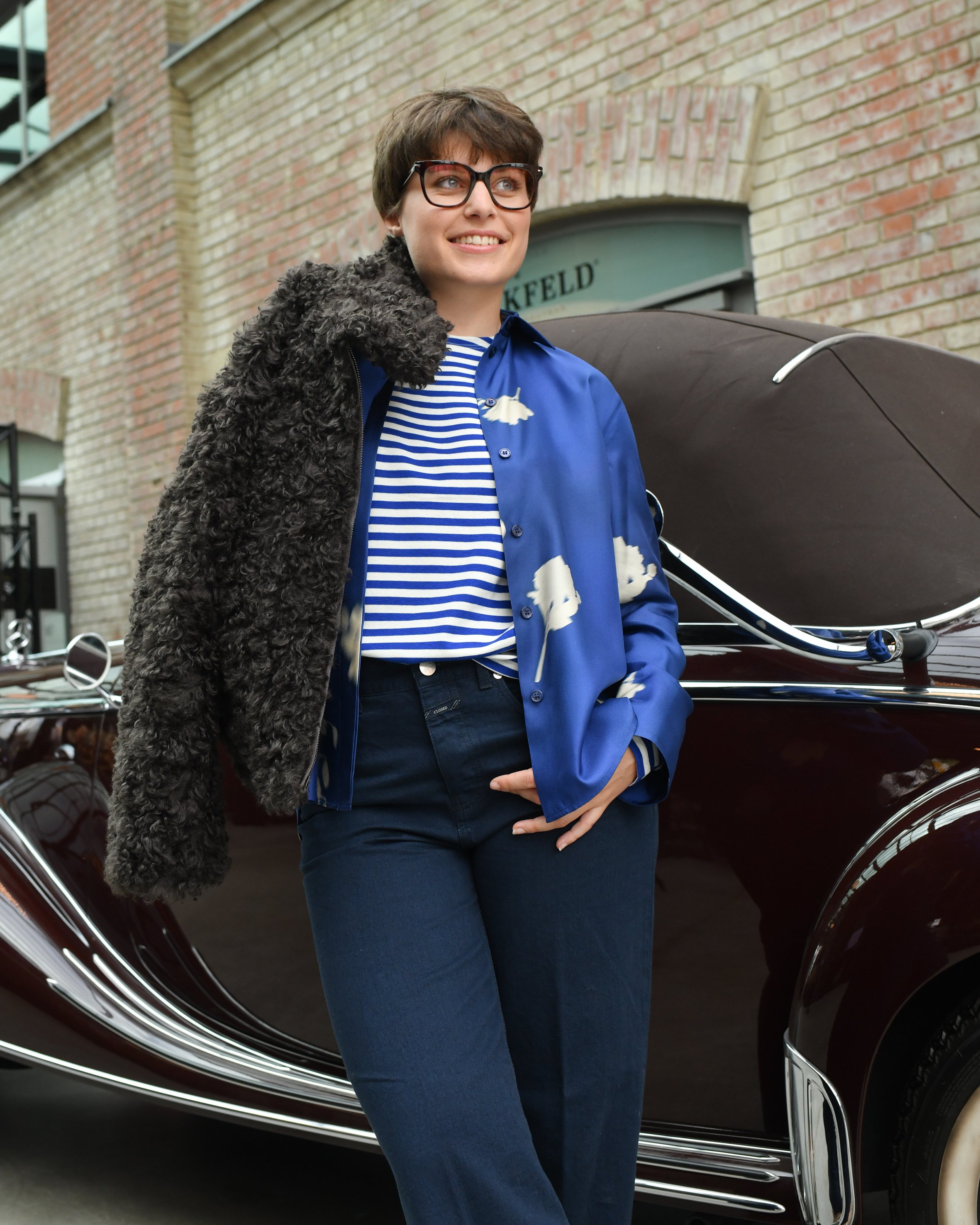 Frau mit dunkelblauer Jeans, blauer Seidenbluse und dunkelbrauner Ksucheljacke
