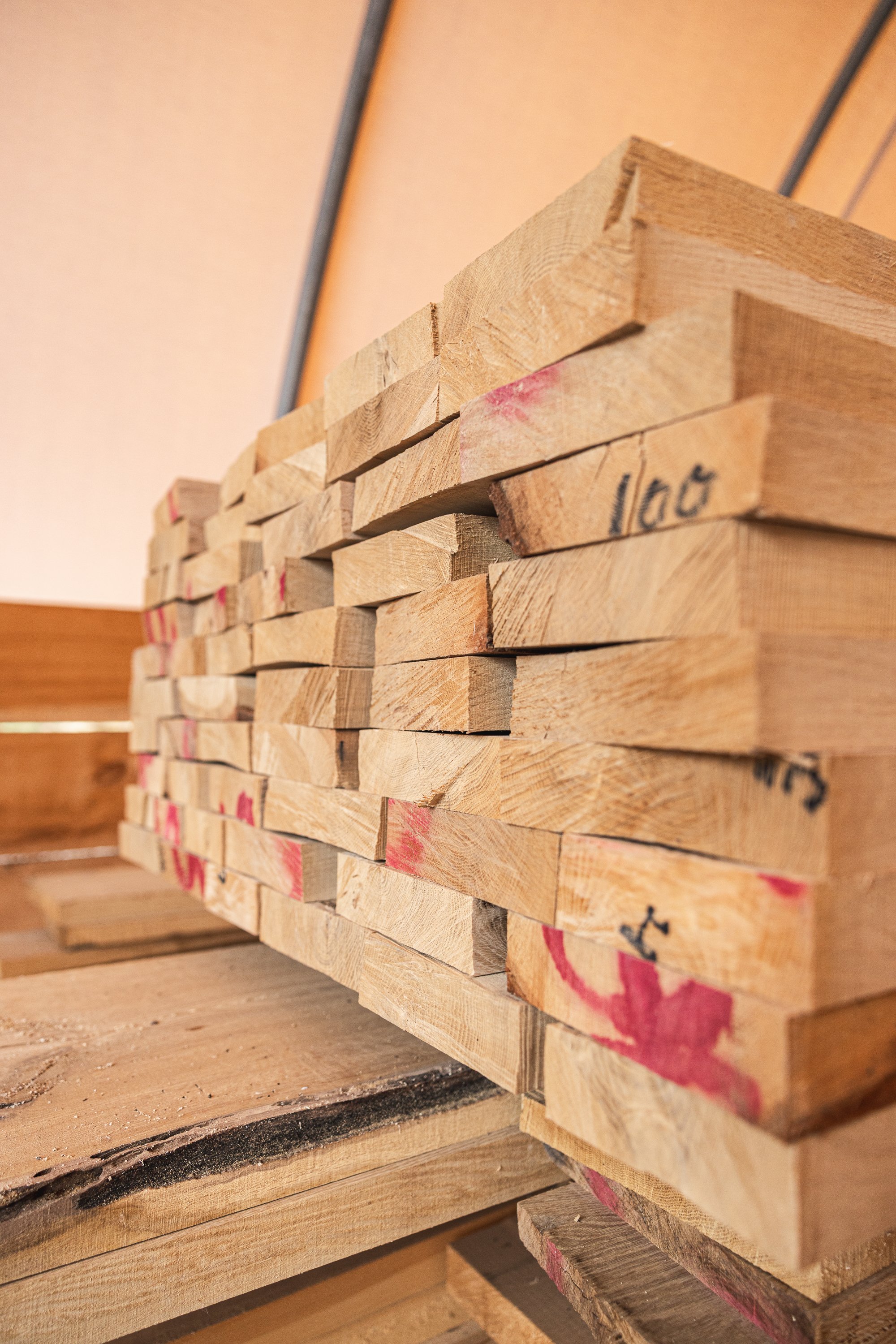 Stacked wooden planks on a pallet, with markings and measurements on some pieces, in a warehouse or workshop setting.