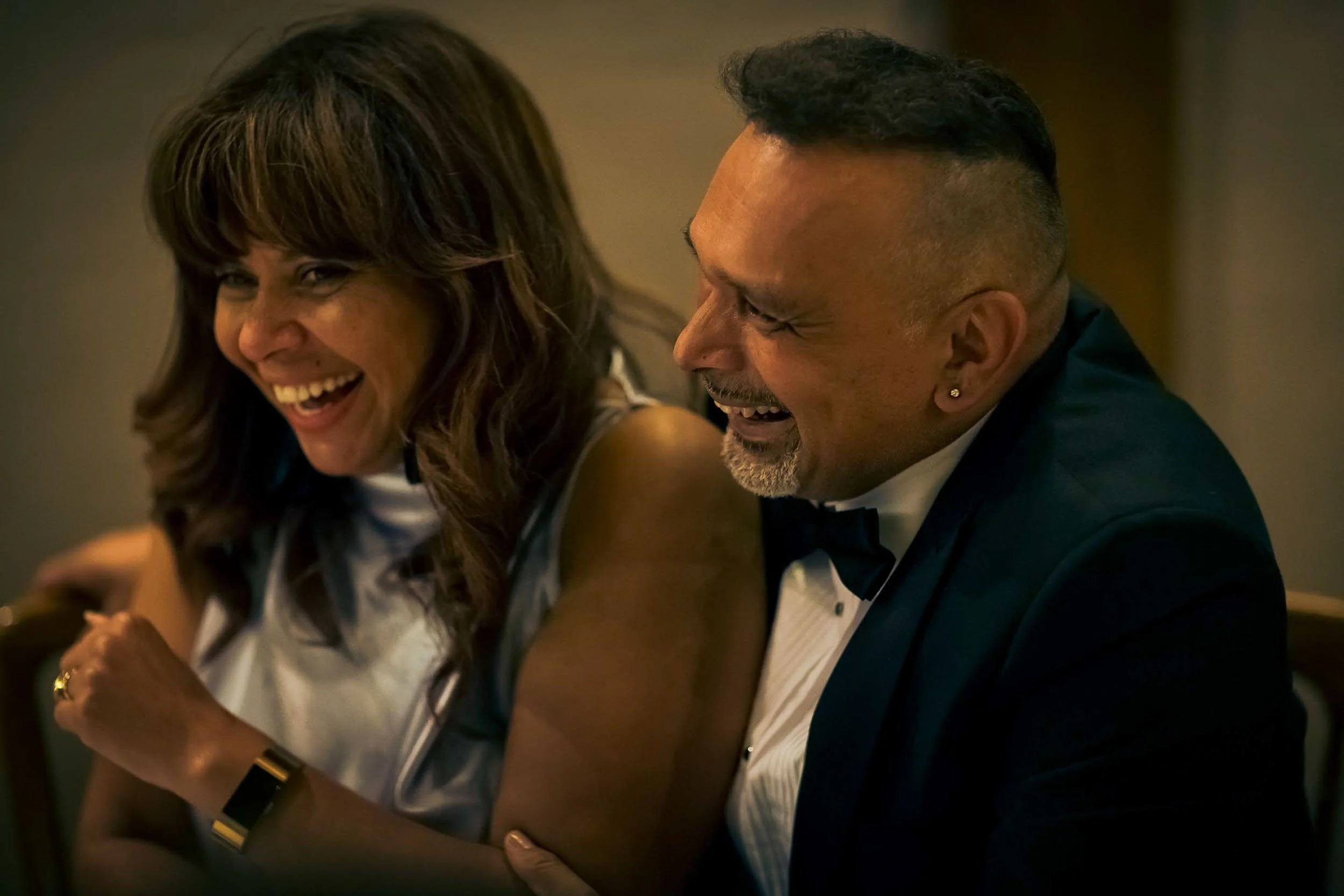 A man and woman dressed in formal attire laughing and enjoying themselves at a social event.