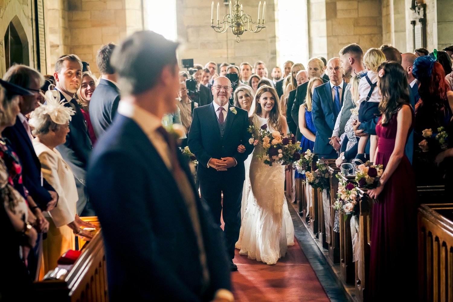 A bride walking down the aisle with her father at a wedding ceremony in a church, surrounded by guests.