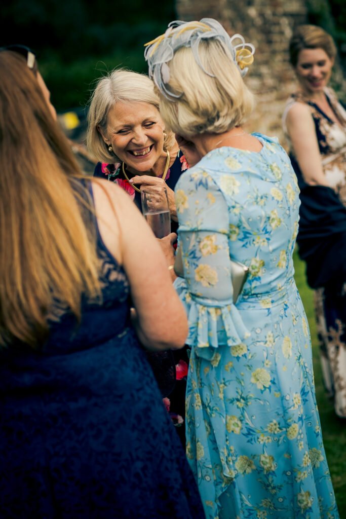 Four women at an outdoor gathering, smiling and talking to each other, dressed in floral and elegant attire.