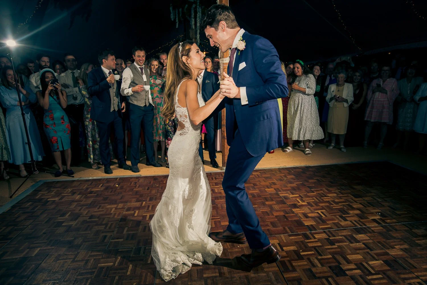 A bride and groom dancing at their wedding reception, surrounded by guests under a decorated tent.