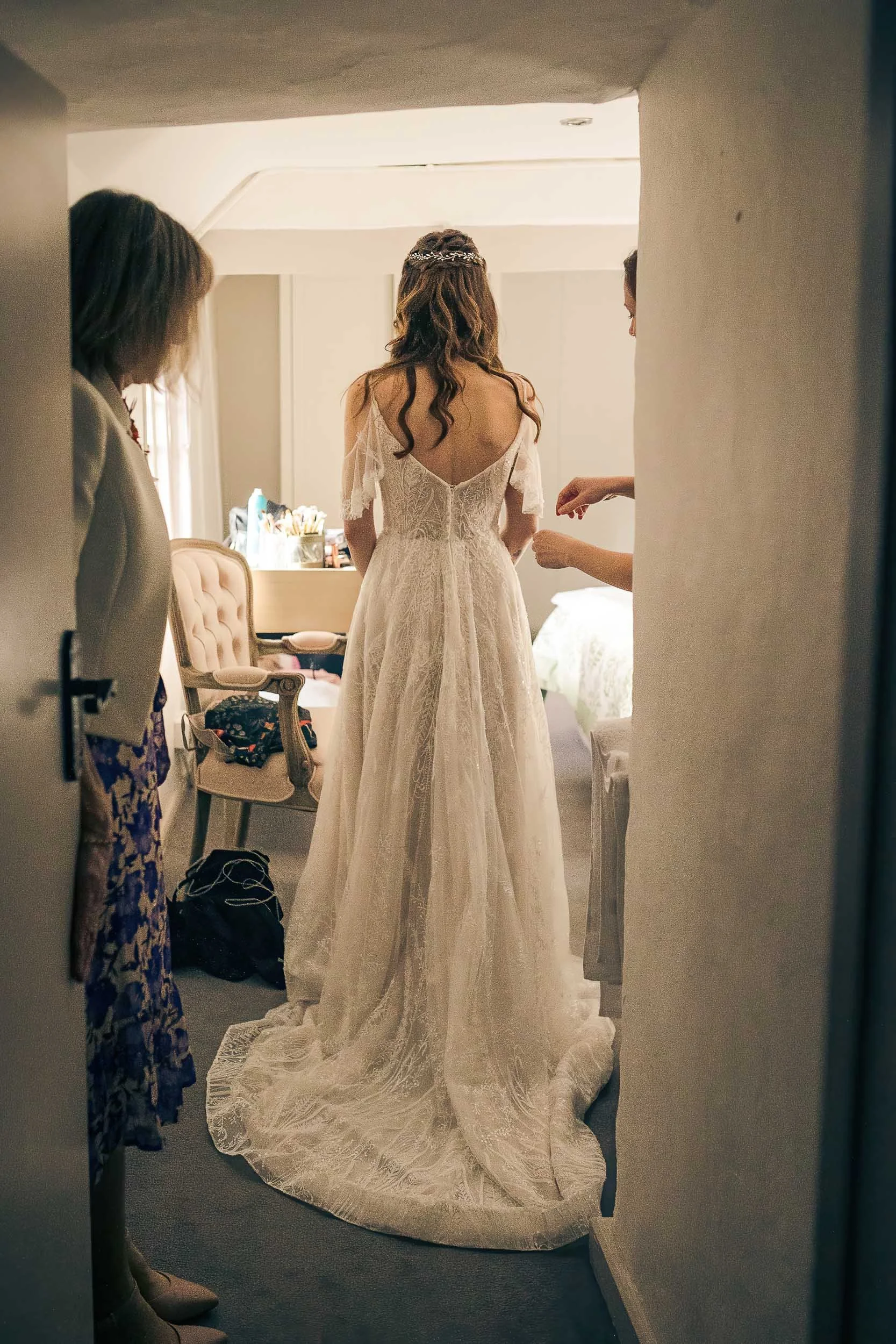 A bride in a white wedding dress standing in a room as her attendants help her get ready.
