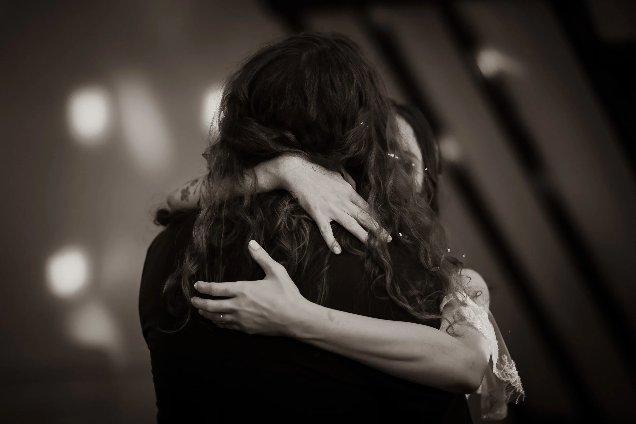Two women embracing each other in a close hug, with their faces hidden, in black and white.