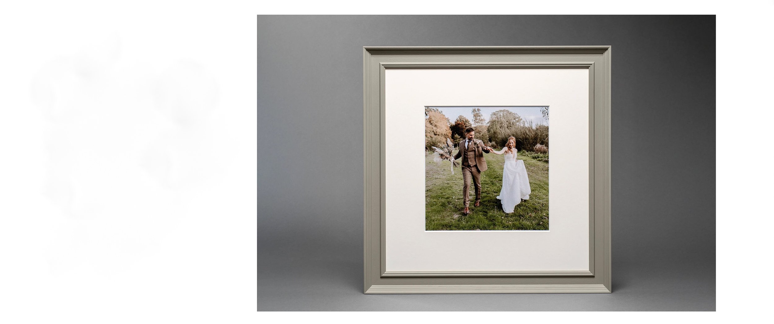 Photograph of a framed wedding picture of a couple walking hand in hand outdoors on green grass with trees in autumn colors in the background.