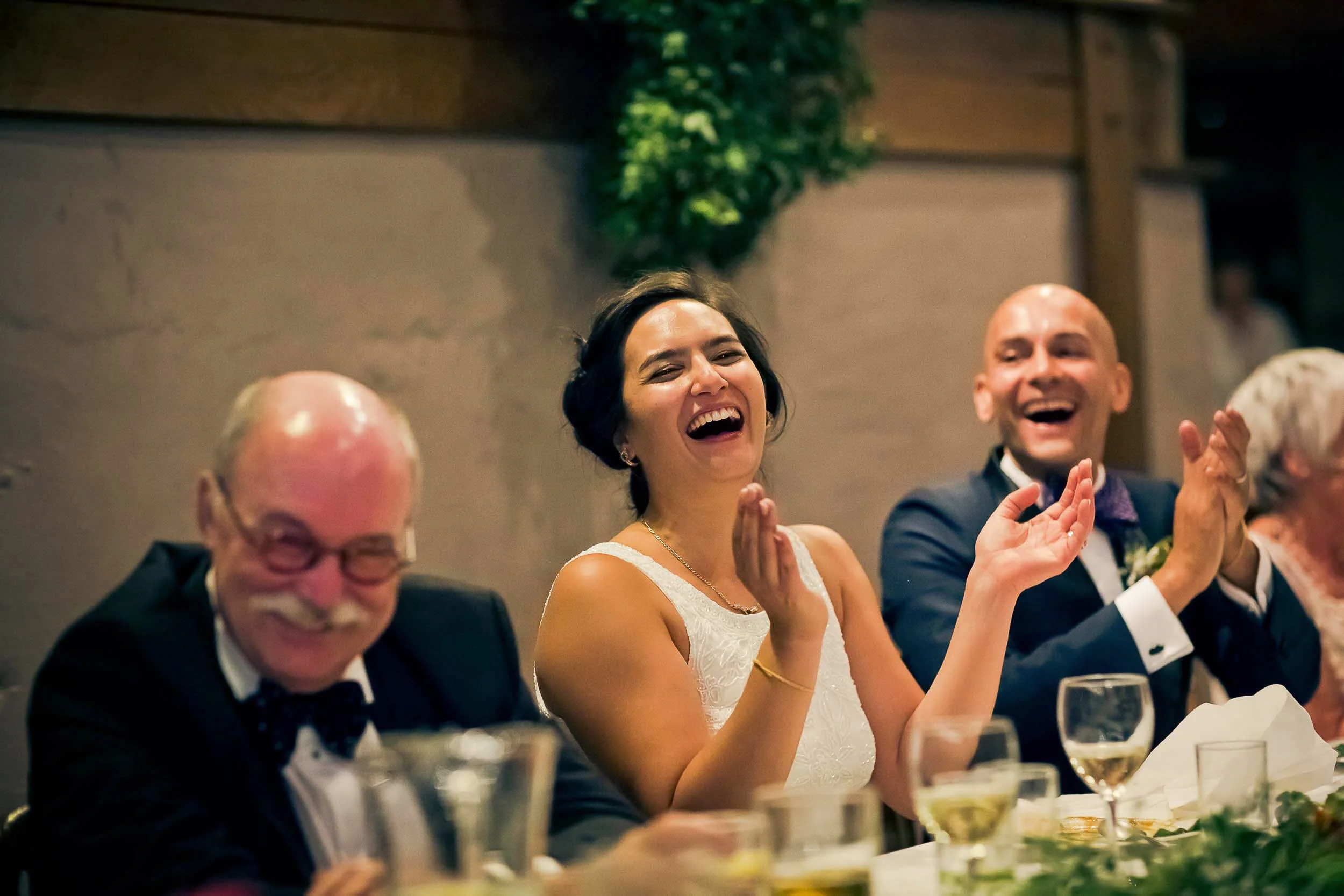 People sitting at a table laughing and clapping at a celebration or wedding reception.