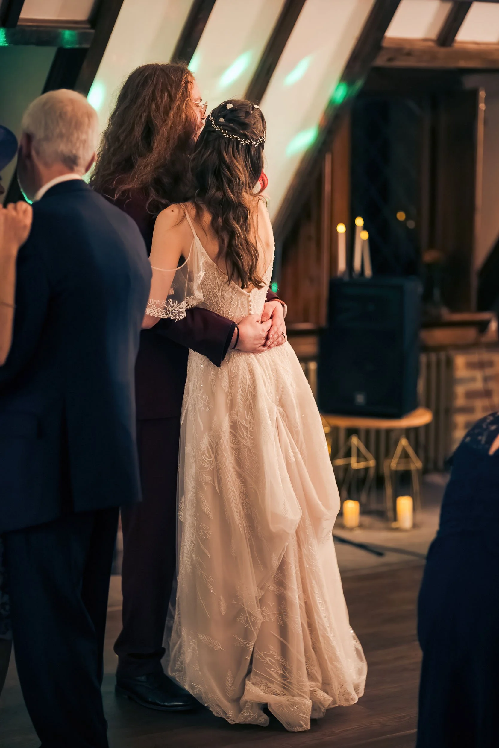 A bride in a gown and a woman holding her at a wedding reception in a rustic venue with candles and candles on stands in the background.