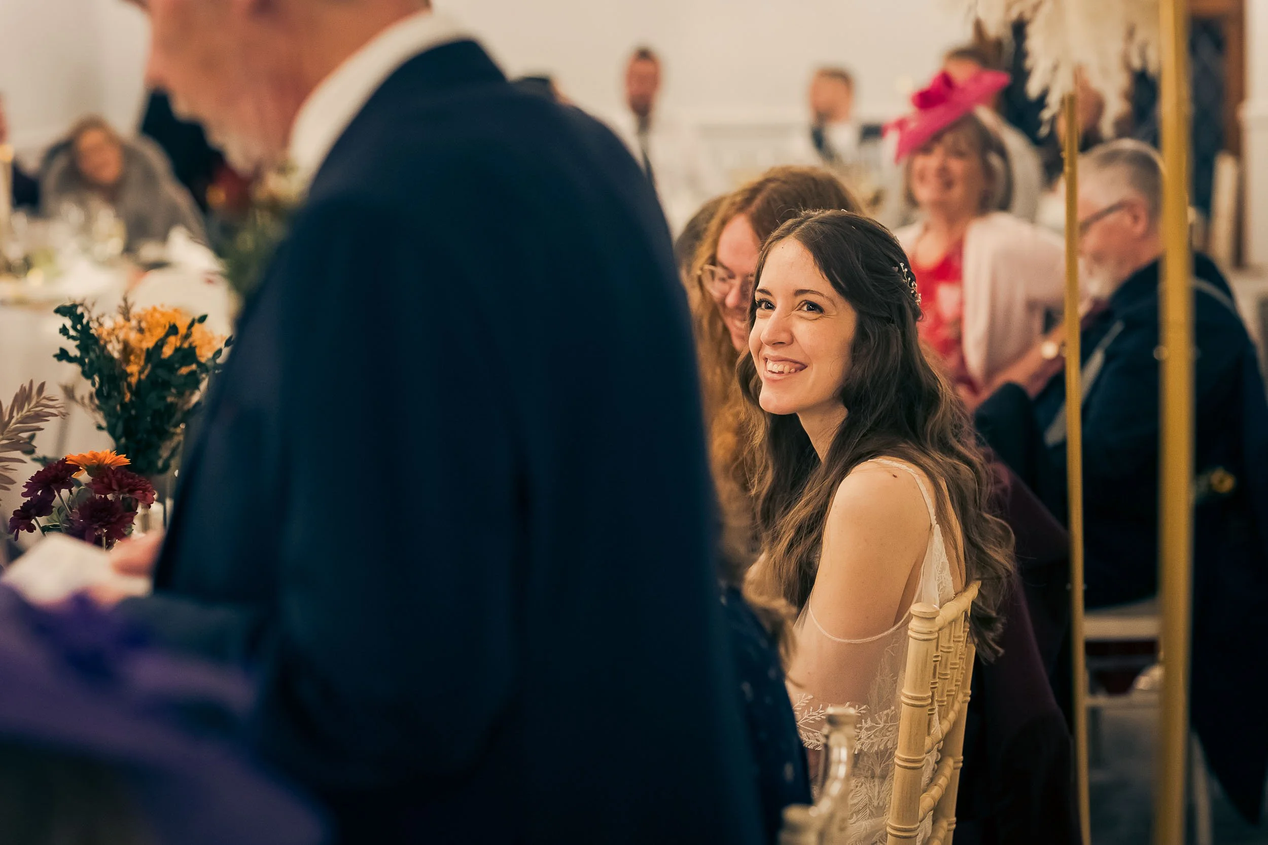 A young woman with long brown hair smiling at a wedding reception.