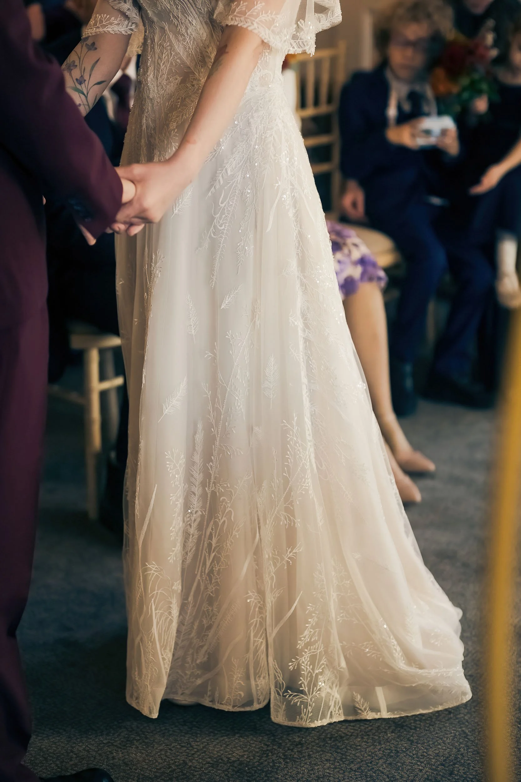 A bride and groom holding hands during a wedding ceremony, with guests seated in the background.