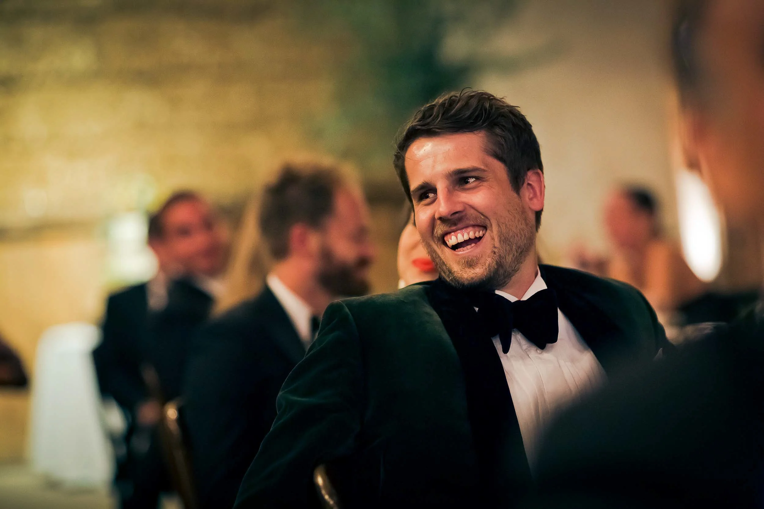 A smiling man in a tuxedo and bow tie at an elegant event or celebration.