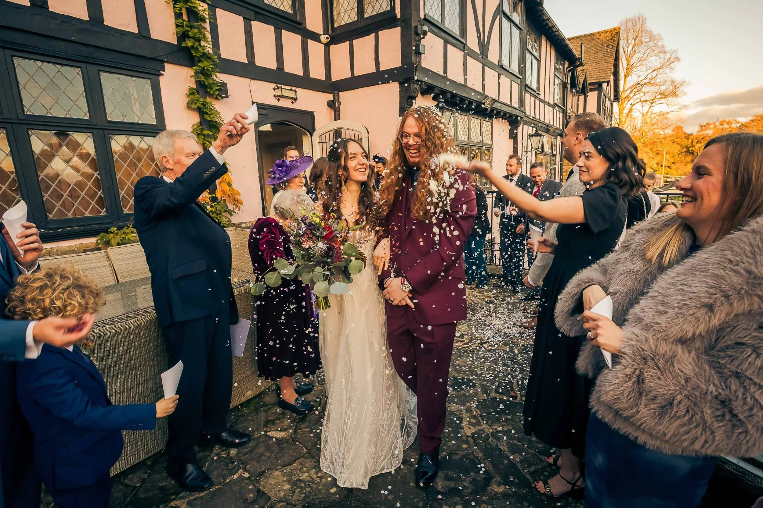 A wedding celebration outside with guests throwing confetti over a bride and groom.