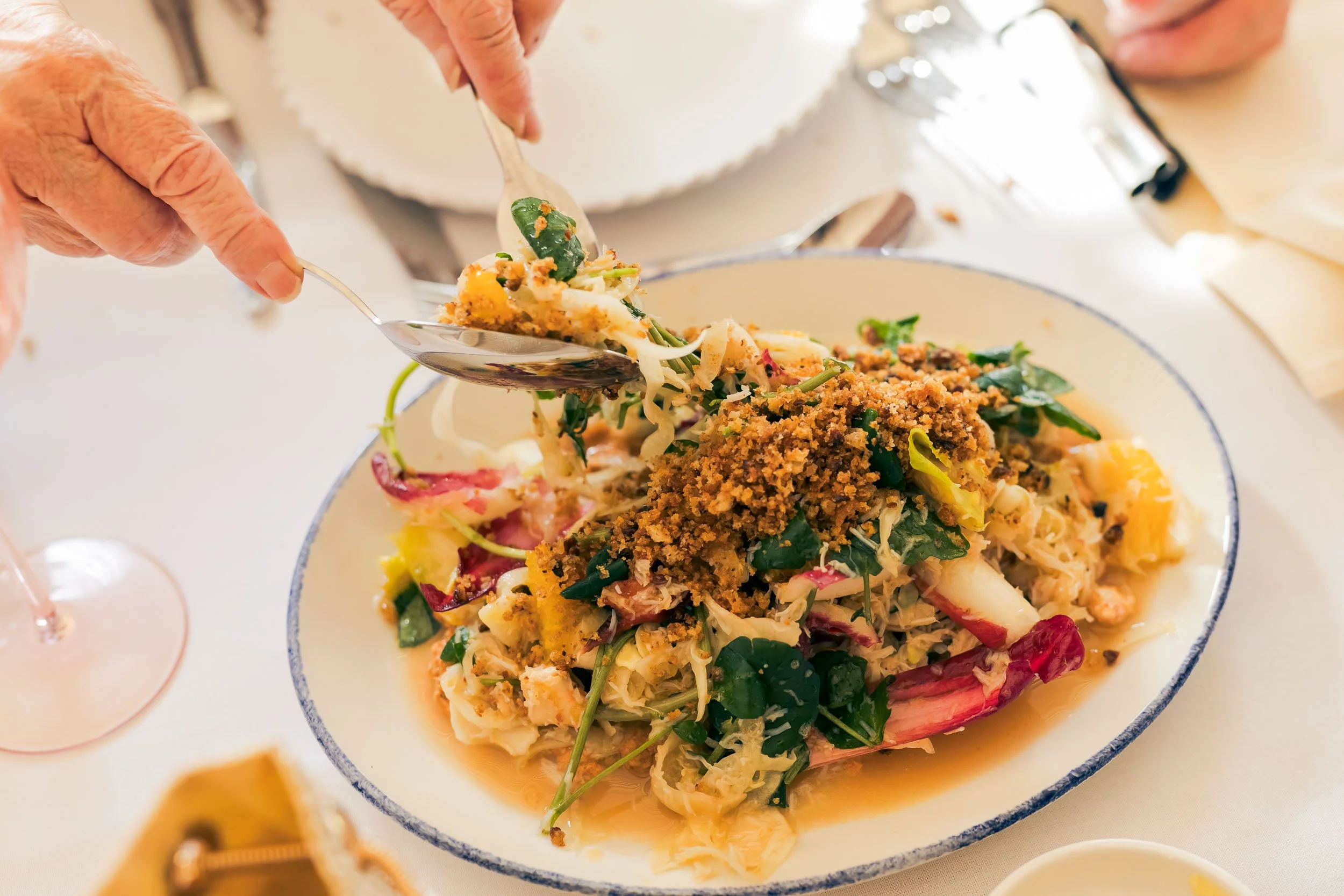 Person serving salad with greens, vegetables, and toppings from a large oval bowl.