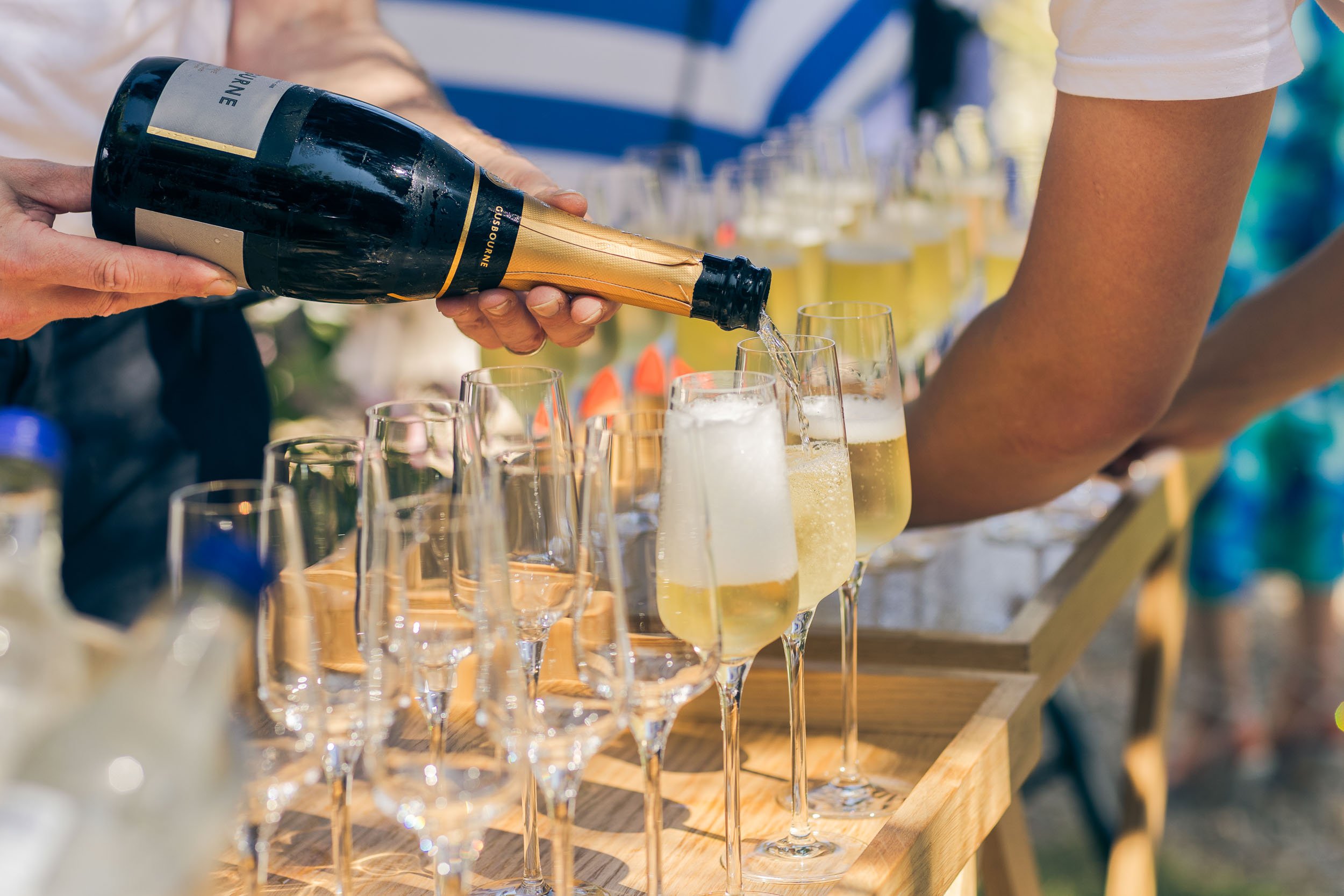 Person pouring champagne into glasses at an outdoor celebration or event.
