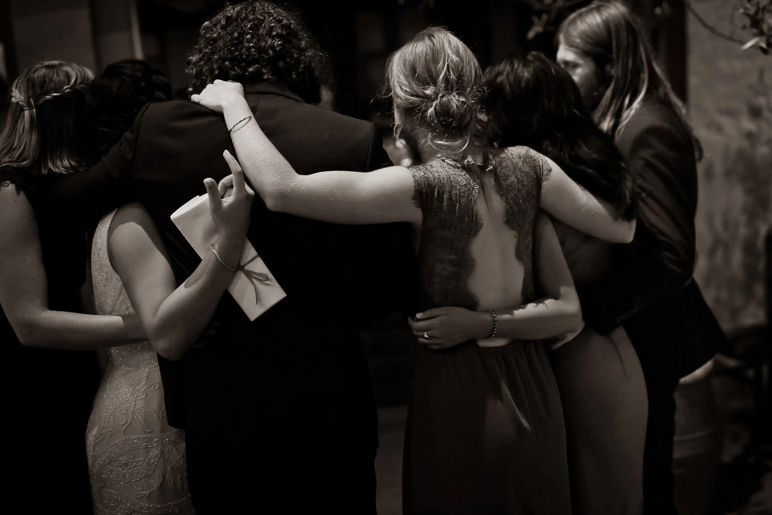 Group of women and a man embracing in a close, intimate hug at a celebration or gathering.
