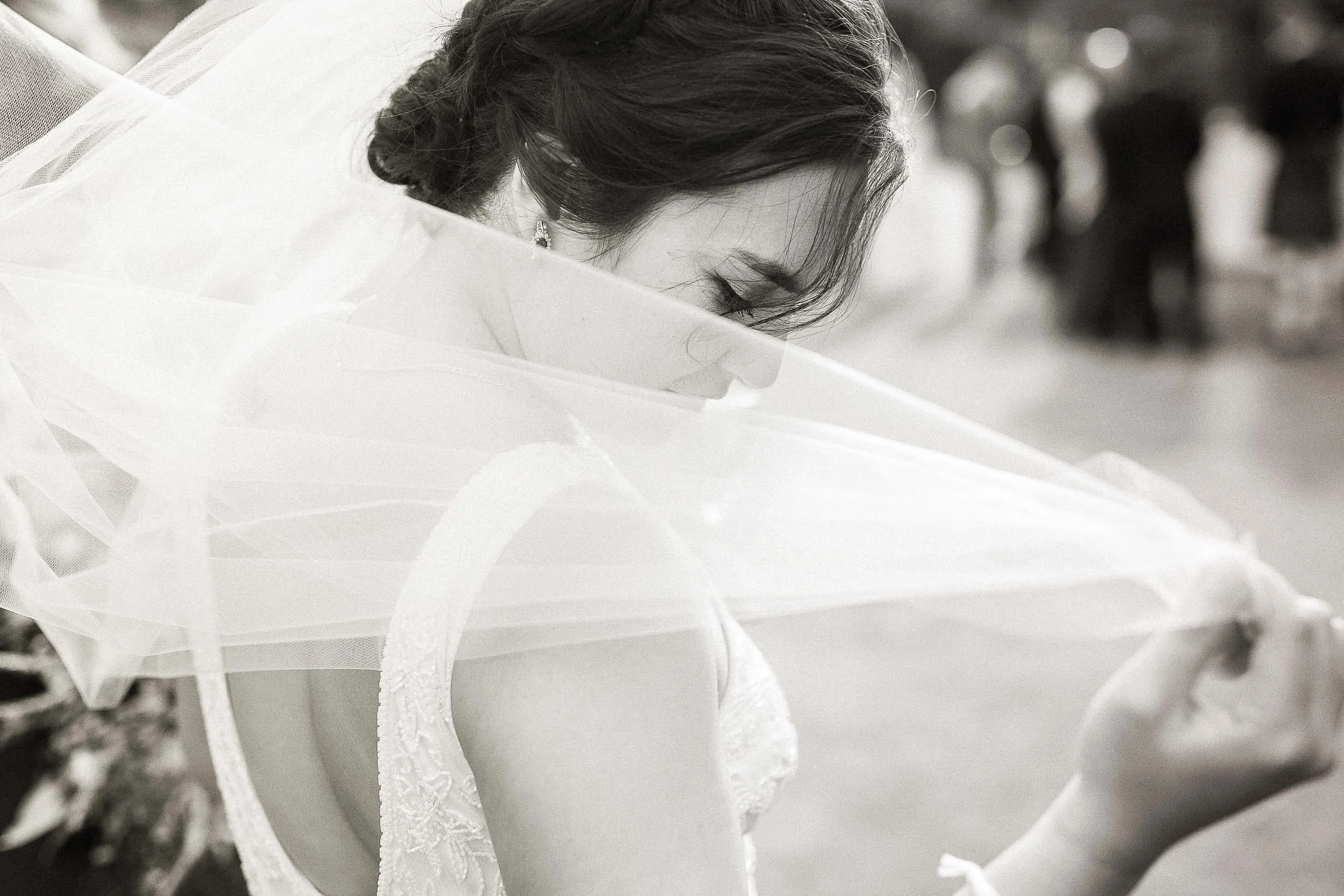 A bride looking down and holding her veil at her wedding.