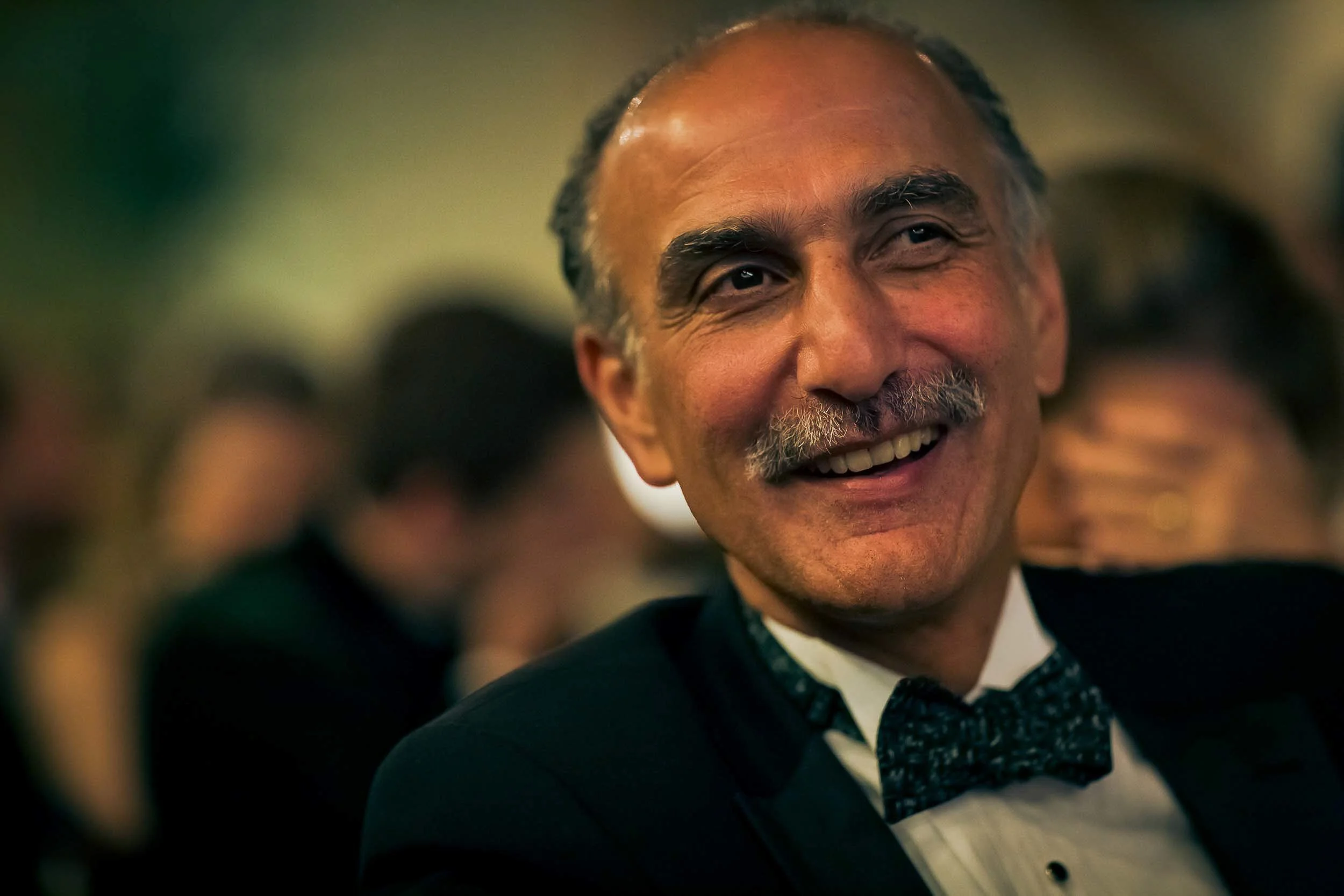 A smiling man with a mustache and gray hair, dressed in formal attire with a bow tie, at a social event.