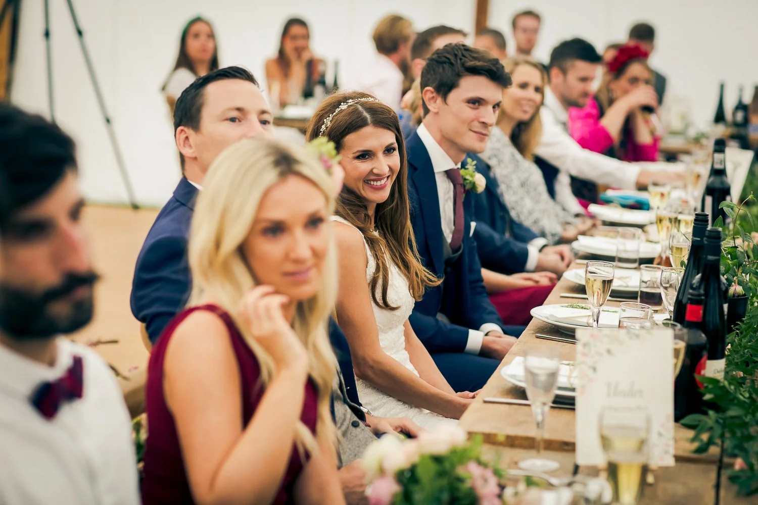 A group of wedding guests seated at a long table, with the bride and groom in the center, smiling and enjoying the celebration.