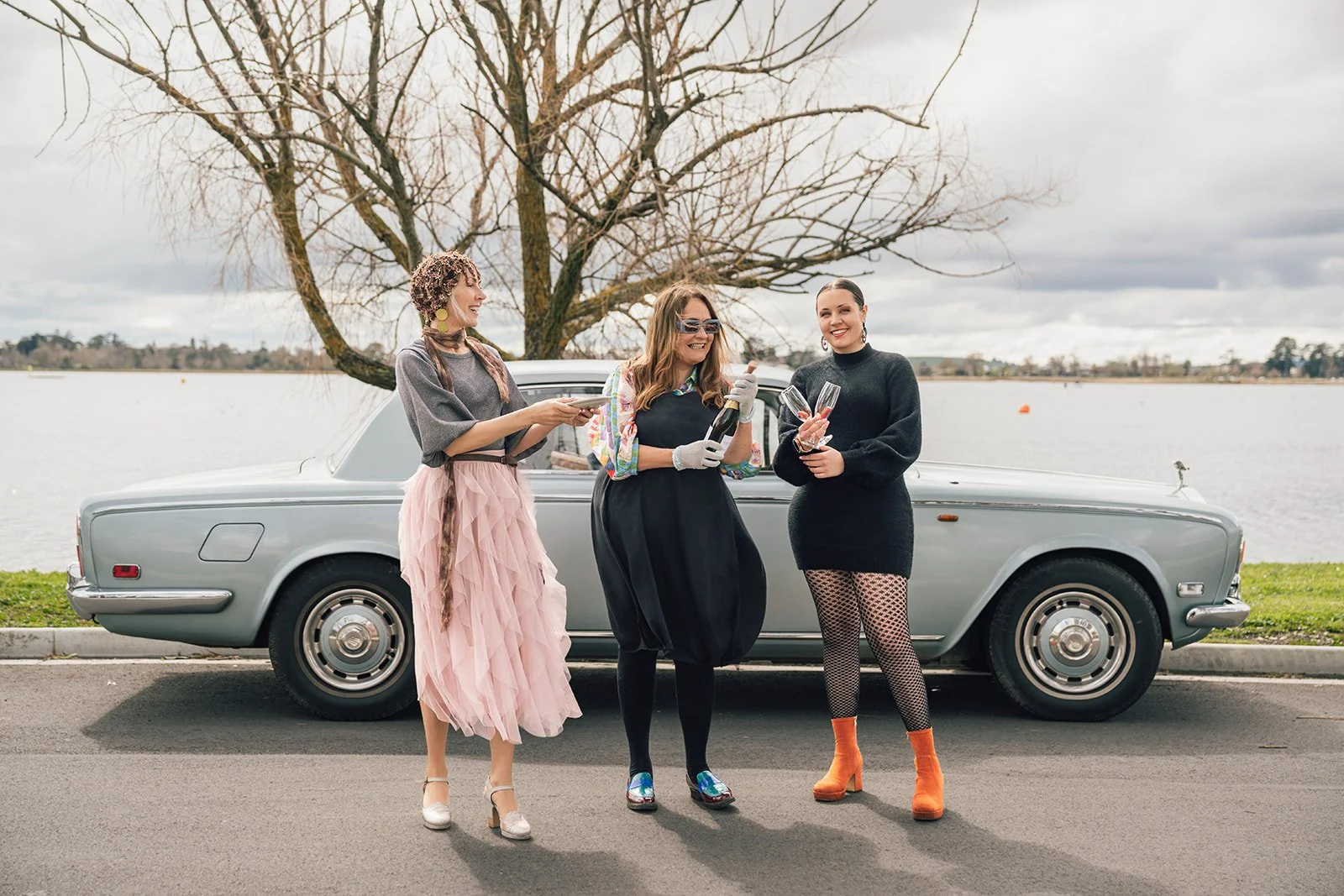 Three women standing in front of a 1974 Silver Shadow vintage Rolls Royce at Lake Wendouree, Ballarat, celebrating with regional sparkling wine.