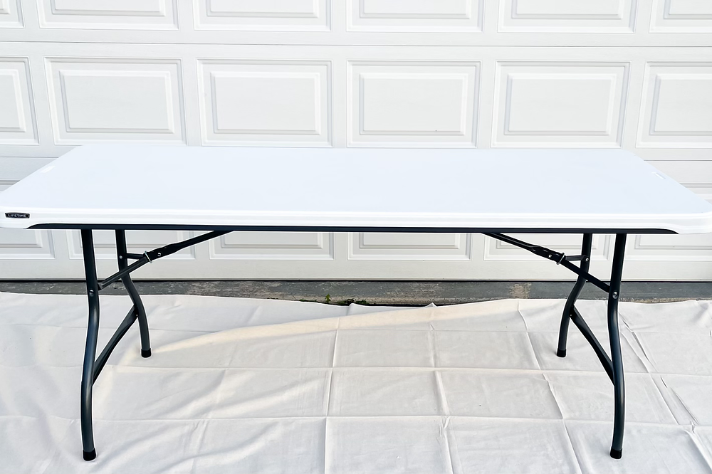 Rectangular folding table with white top and black metal legs against a white garage door.