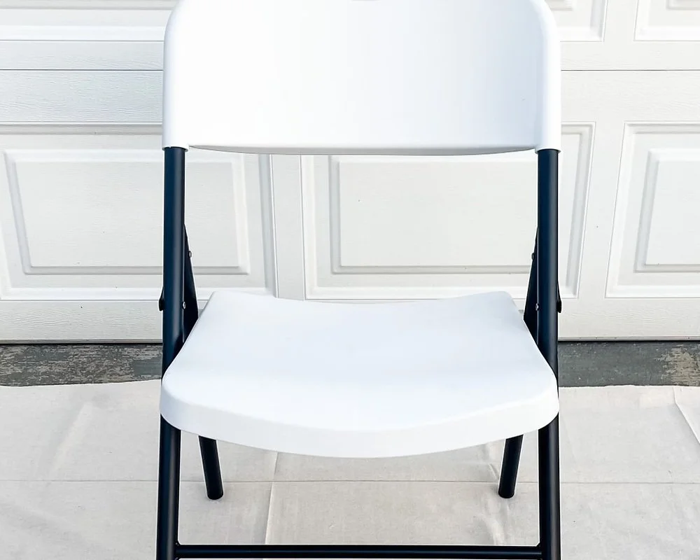 White folding chair with black metal frame in front of garage door