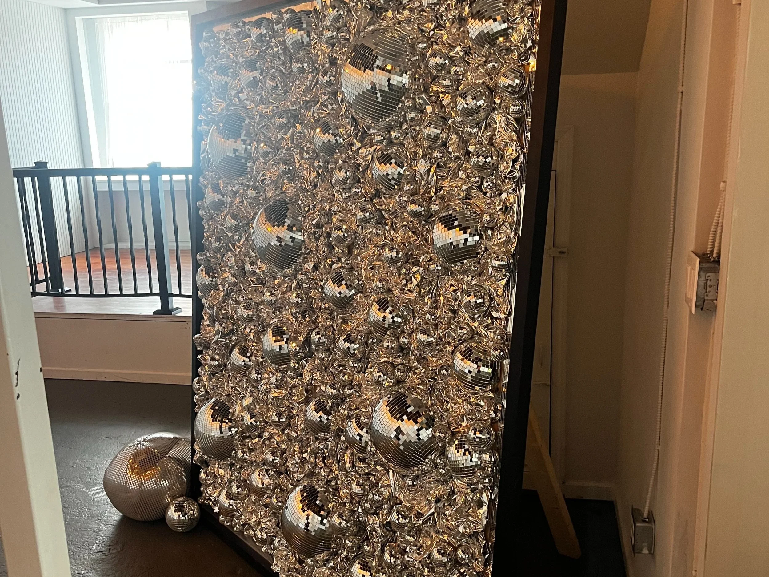 Wall display covered with silver disco balls and reflective material.