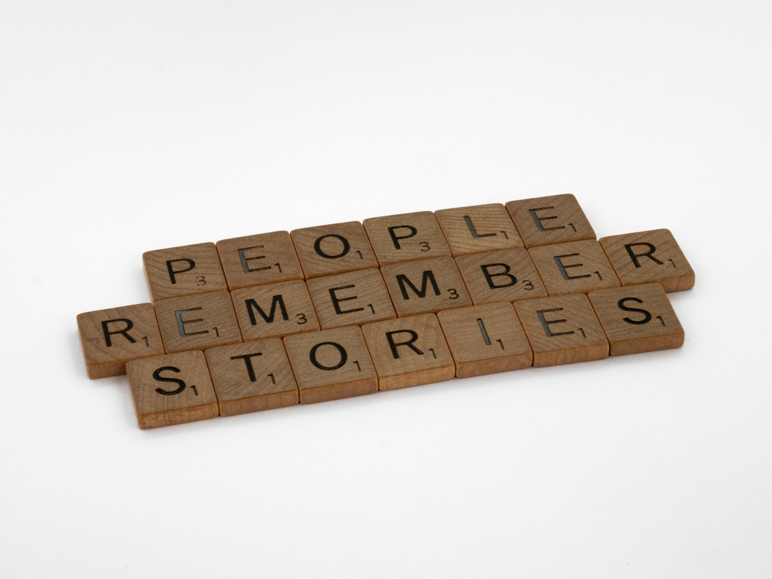 Scrabble tiles spelling out "PEOPLE REMEMBER STORIES" on a white background.