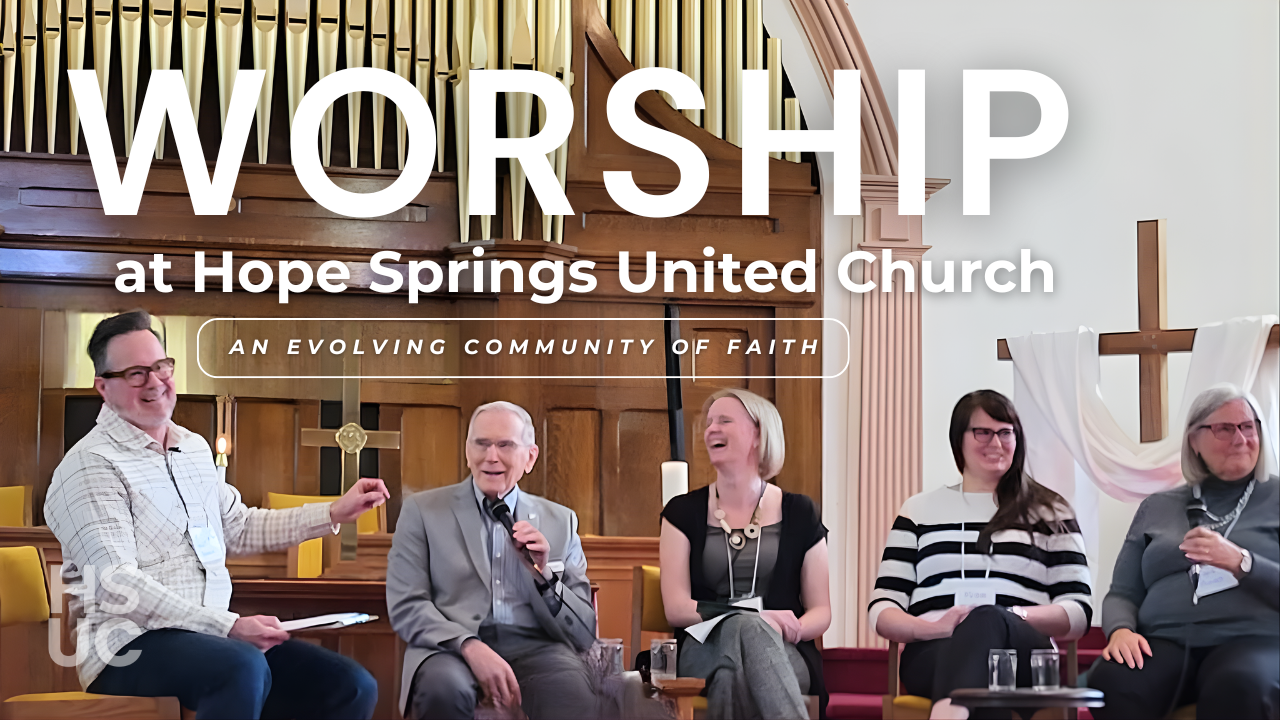 Five people sit on chairs at the front of a church sanctuary. They are laughing together. An elderly gentleman is speaking into a microphone.