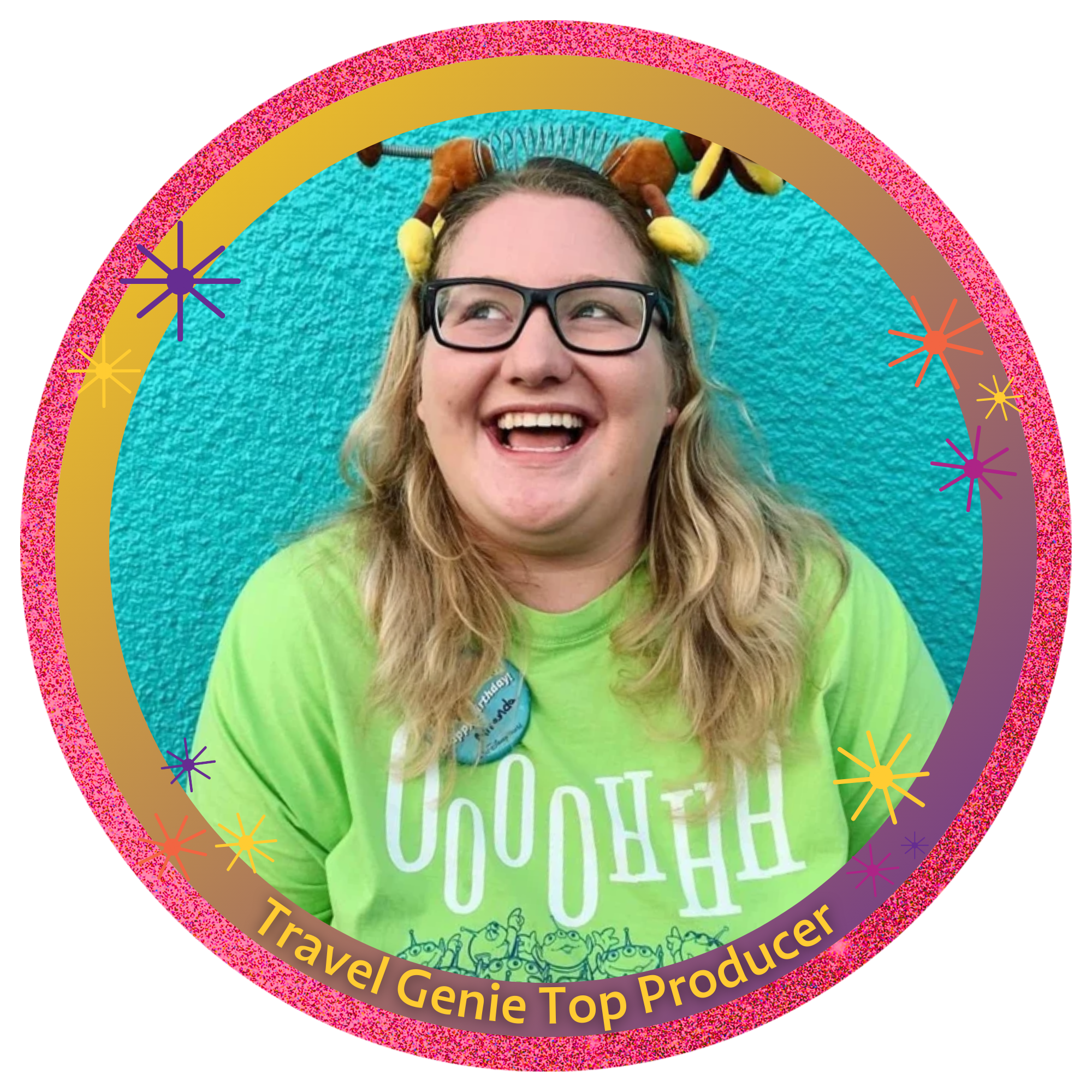 A woman with glasses and blonde hair, smiling and looking to her left, standing against a teal textured wall. She is wearing a bright green T-shirt with a graphic of cartoon characters and a button that says 'Happy Birthday.' She has a plush dog headband on her head.