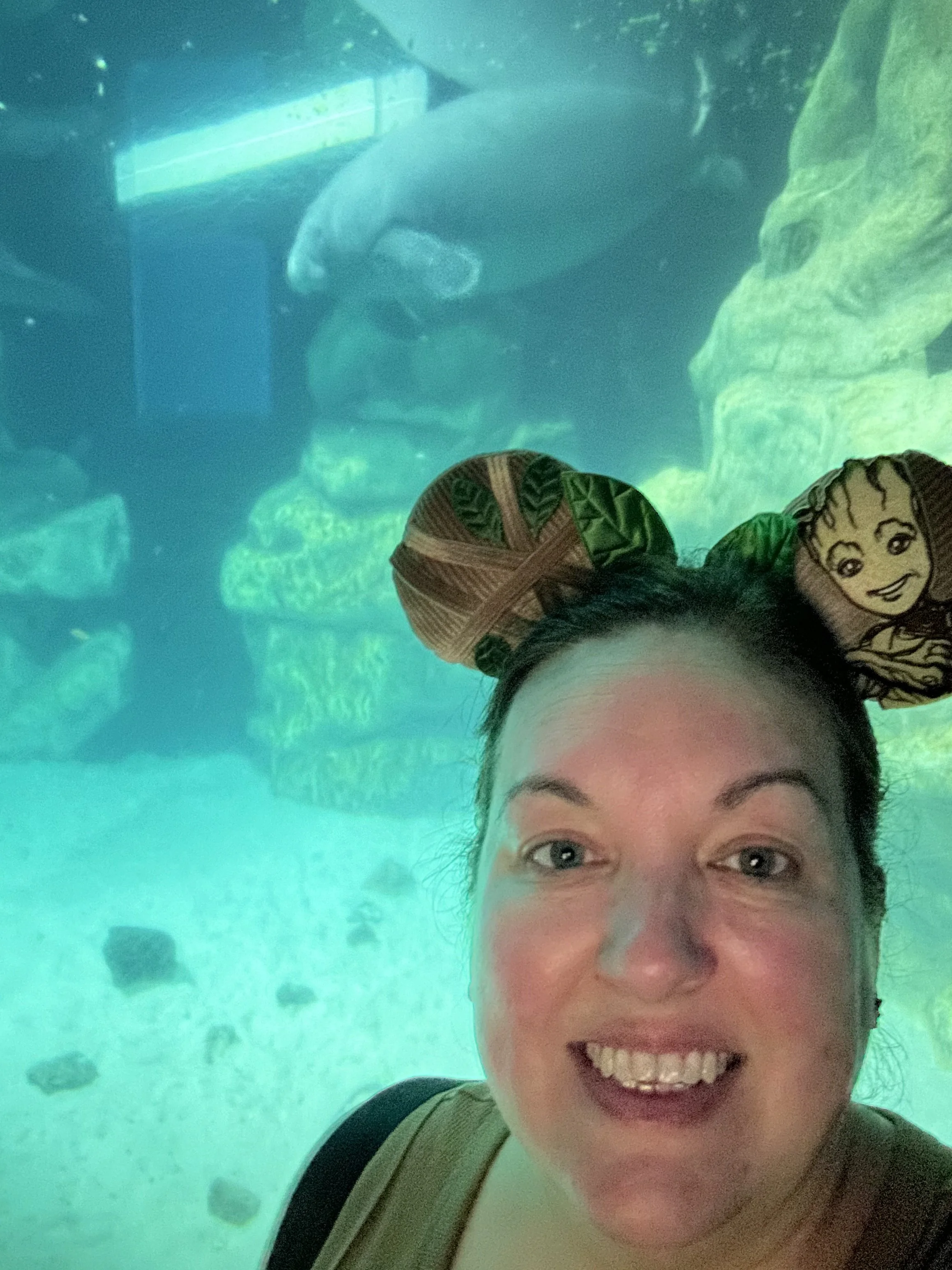 A woman taking a selfie at an aquarium, with a large fish or shark behind the glass in the background.