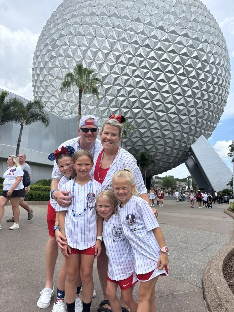 Family of five posing in front of Spaceship Earth at EPCOT, Disney World, wearing matching baseball jerseys with personalized names and Mickey Mouse ears, with other park visitors in the background.