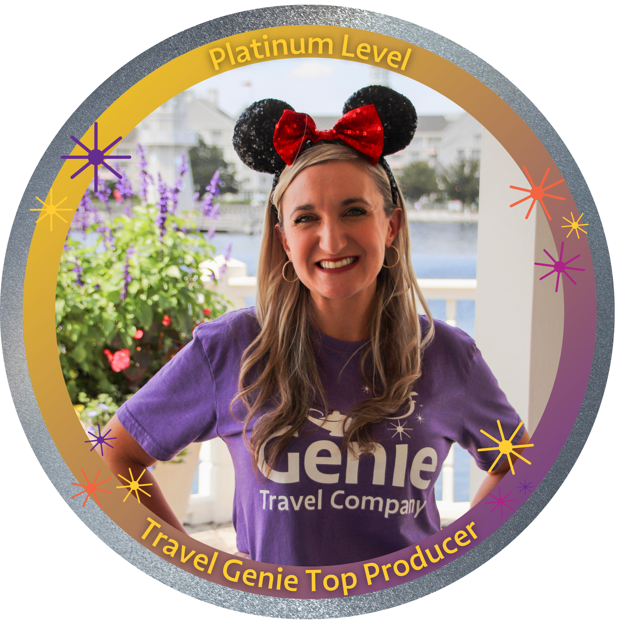 Woman smiling, wearing a purple 'Travel Genie' T-shirt and Disney mouse ears headband, standing outdoors with flowers and water in the background.