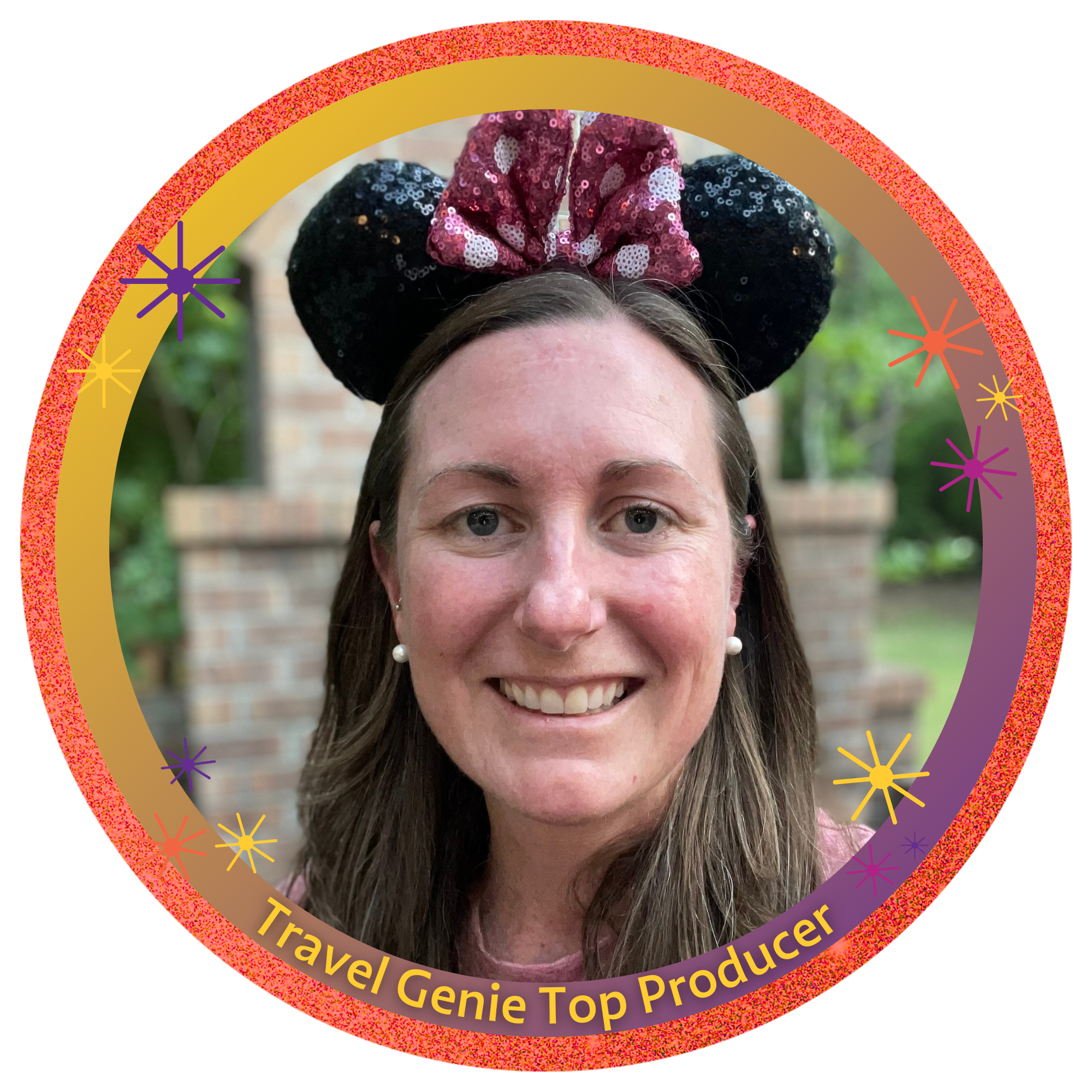 A woman with long brown hair, wearing pearl earrings, smiling, and wearing Minnie Mouse ears with sequins, in front of a brick outdoor fireplace and green foliage.