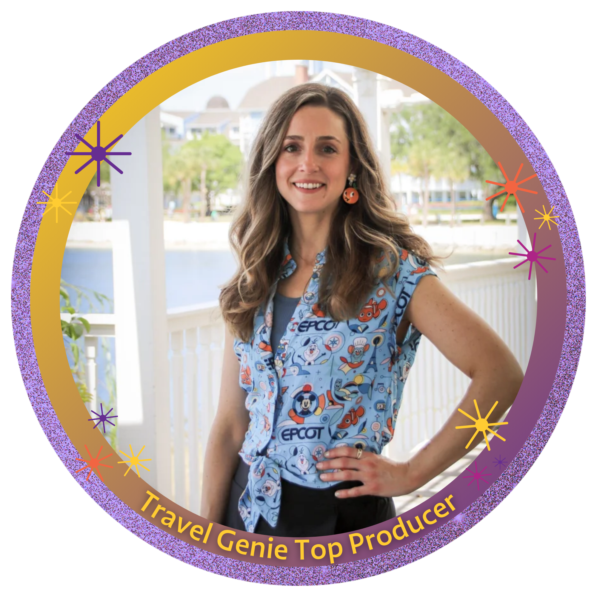 A woman with long wavy brown hair, wearing a Disney-themed sleeveless shirt, stands on a porch by a body of water with houses in the background. She is smiling, with one hand on her hip, and outdoor trees are visible.