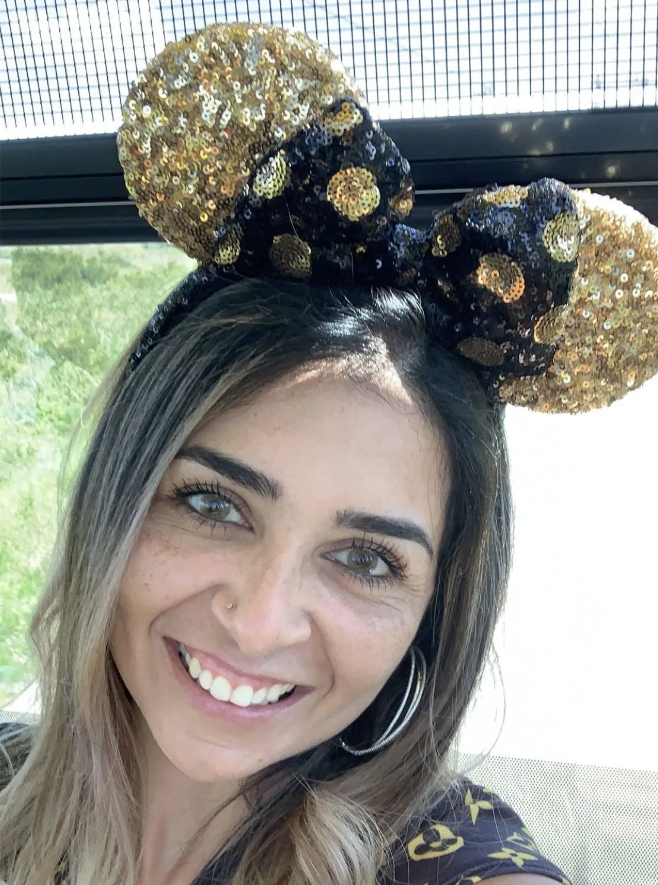 A woman wearing Minnie Mouse ears with gold and black sequins, smiling at the camera.