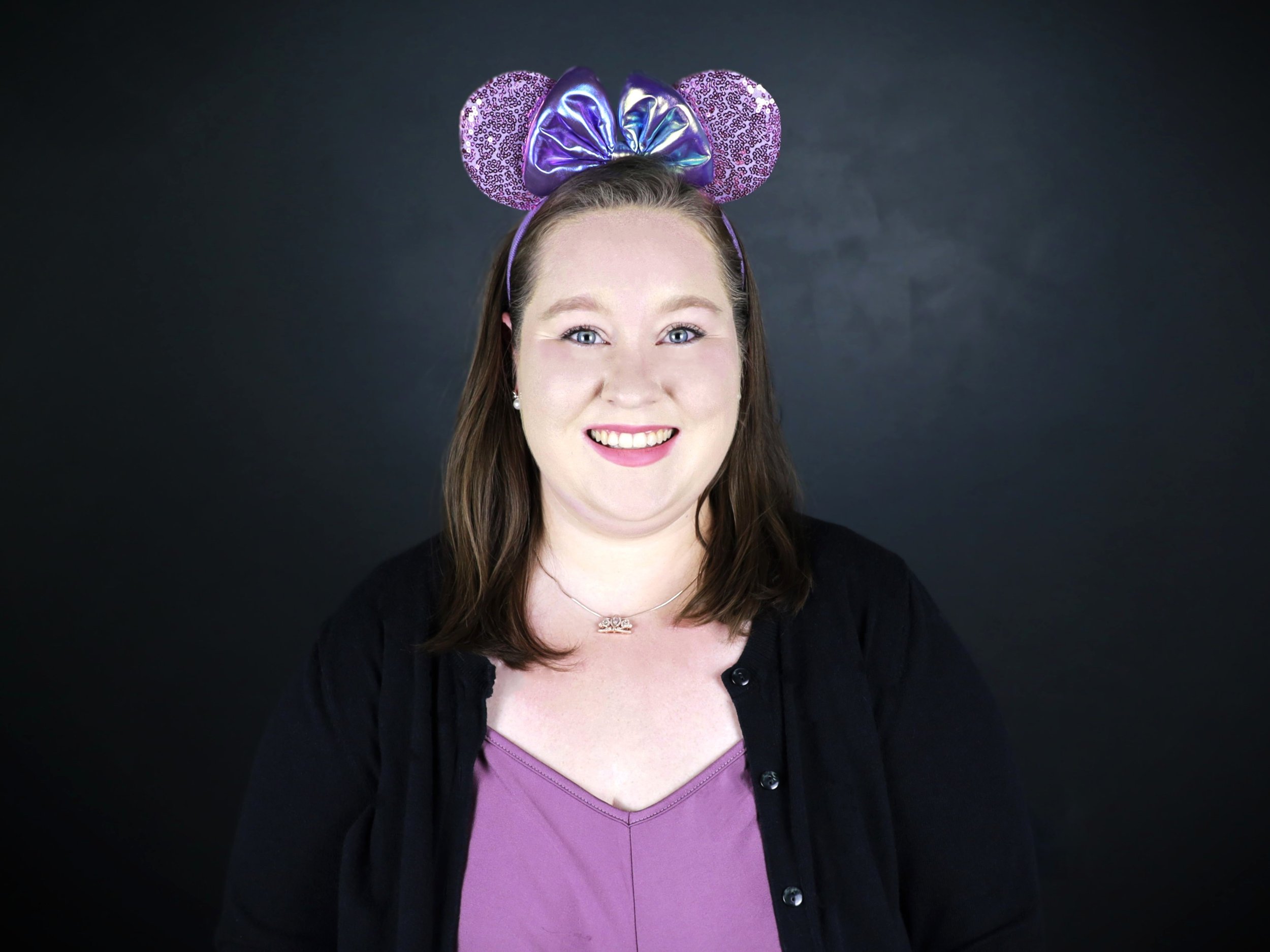 Person smiling standing in front of Disney's Hollywood Studios entrance wearing Minnie Mouse ears headband, yellow patterned shirt, red shorts, and sneakers.