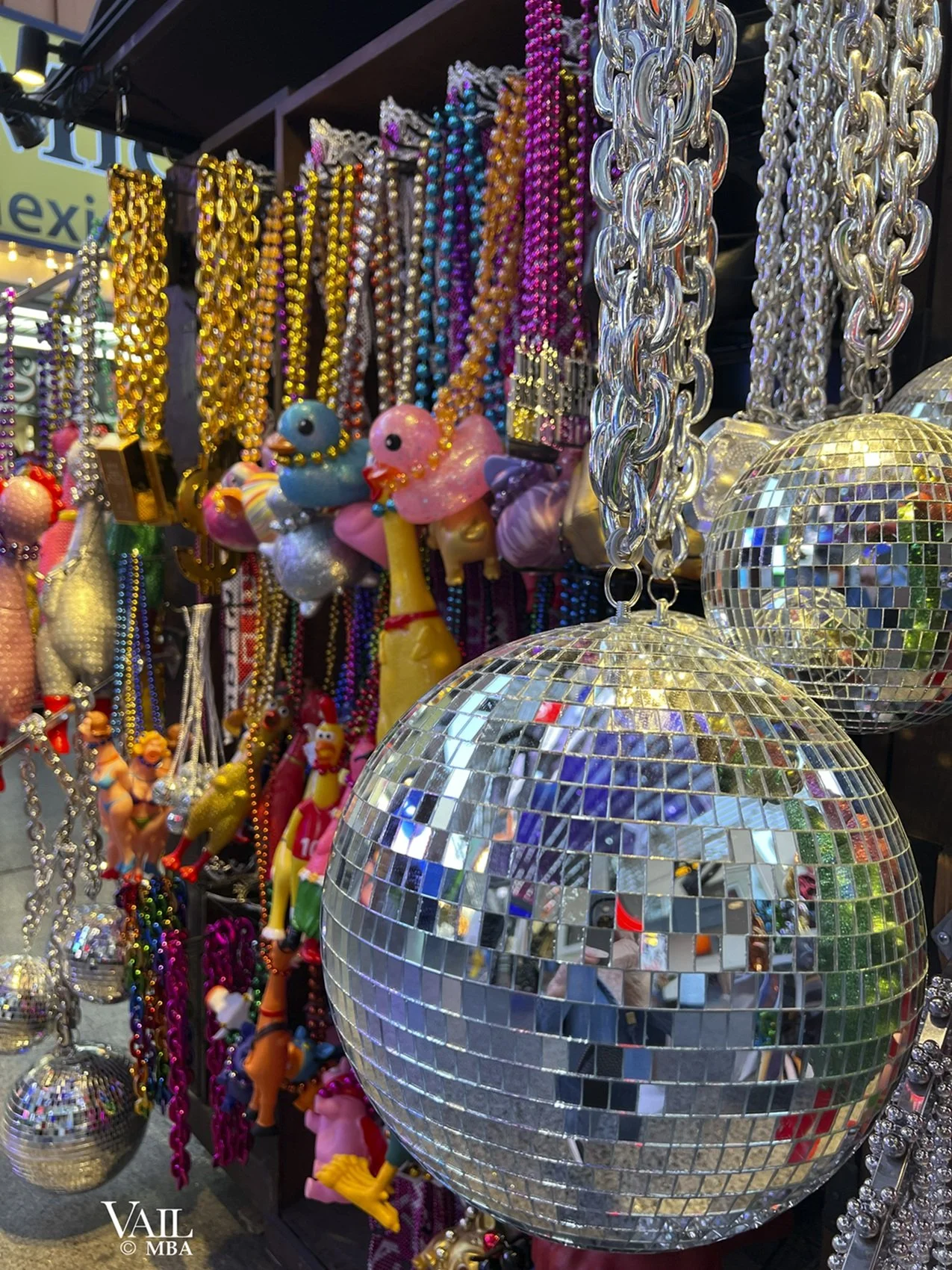 A display of colorful beaded necklaces, small plush duck toys, and disco balls with mirrors reflecting colorful light at a market stall on Freemont Street