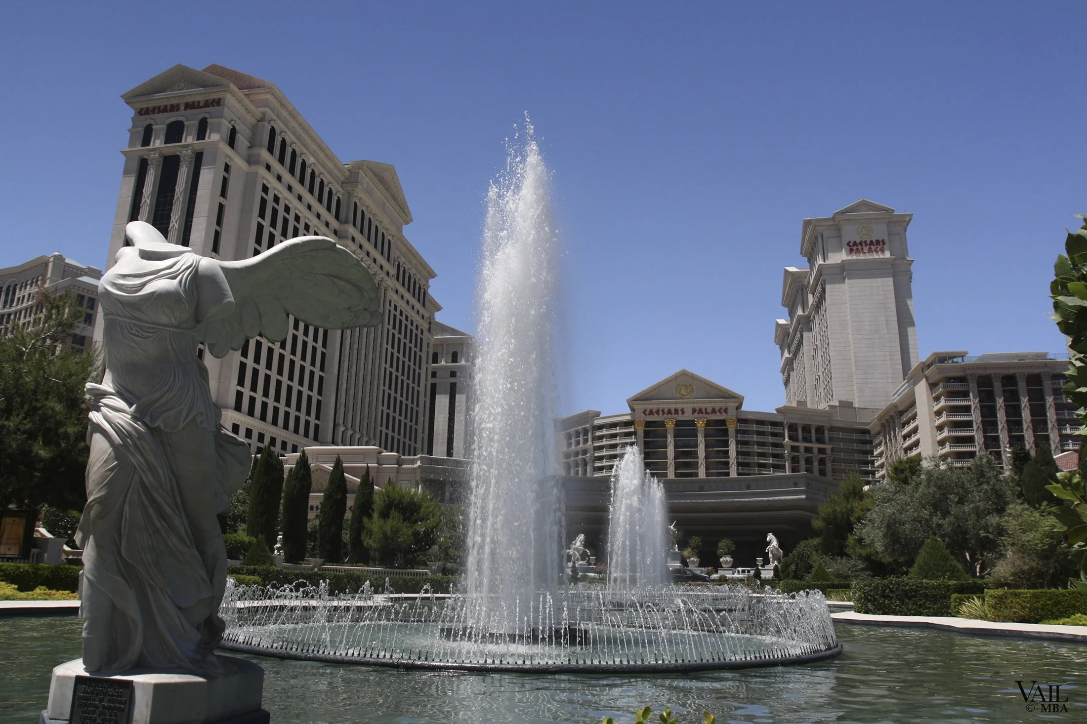 Day photo of  winged figure statue and fountain in front of Caesars Palace hotel and casino in Las Vegas, with clear blue sky.