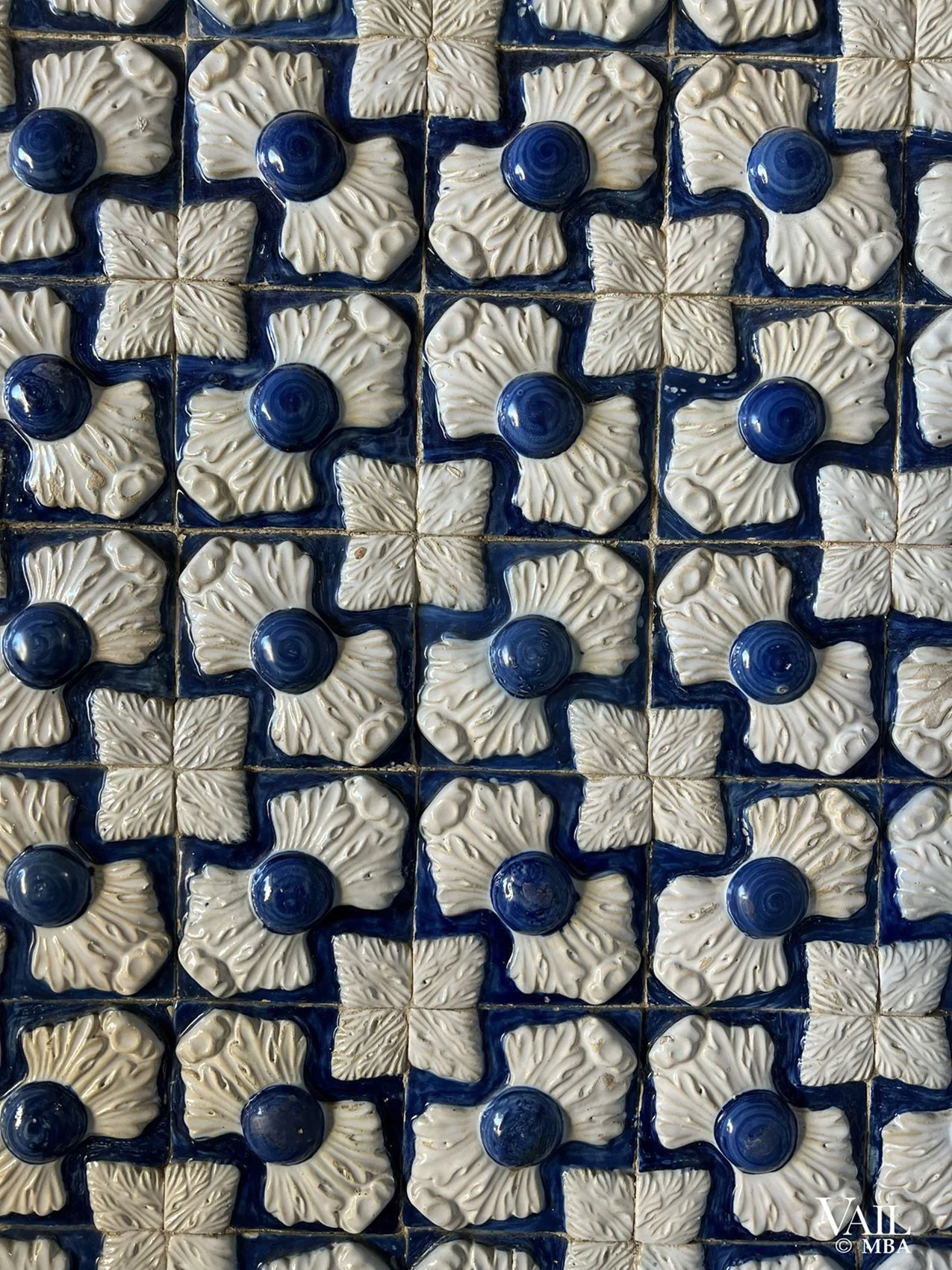 Pattern of decorative ceramic tiles with cream-colored floral designs and blue circular centers, Portugal.