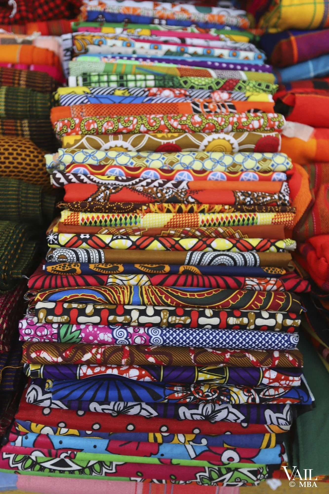 Stack of colorful, patterned African fabrics with various designs and colors on display in a Kenya market.