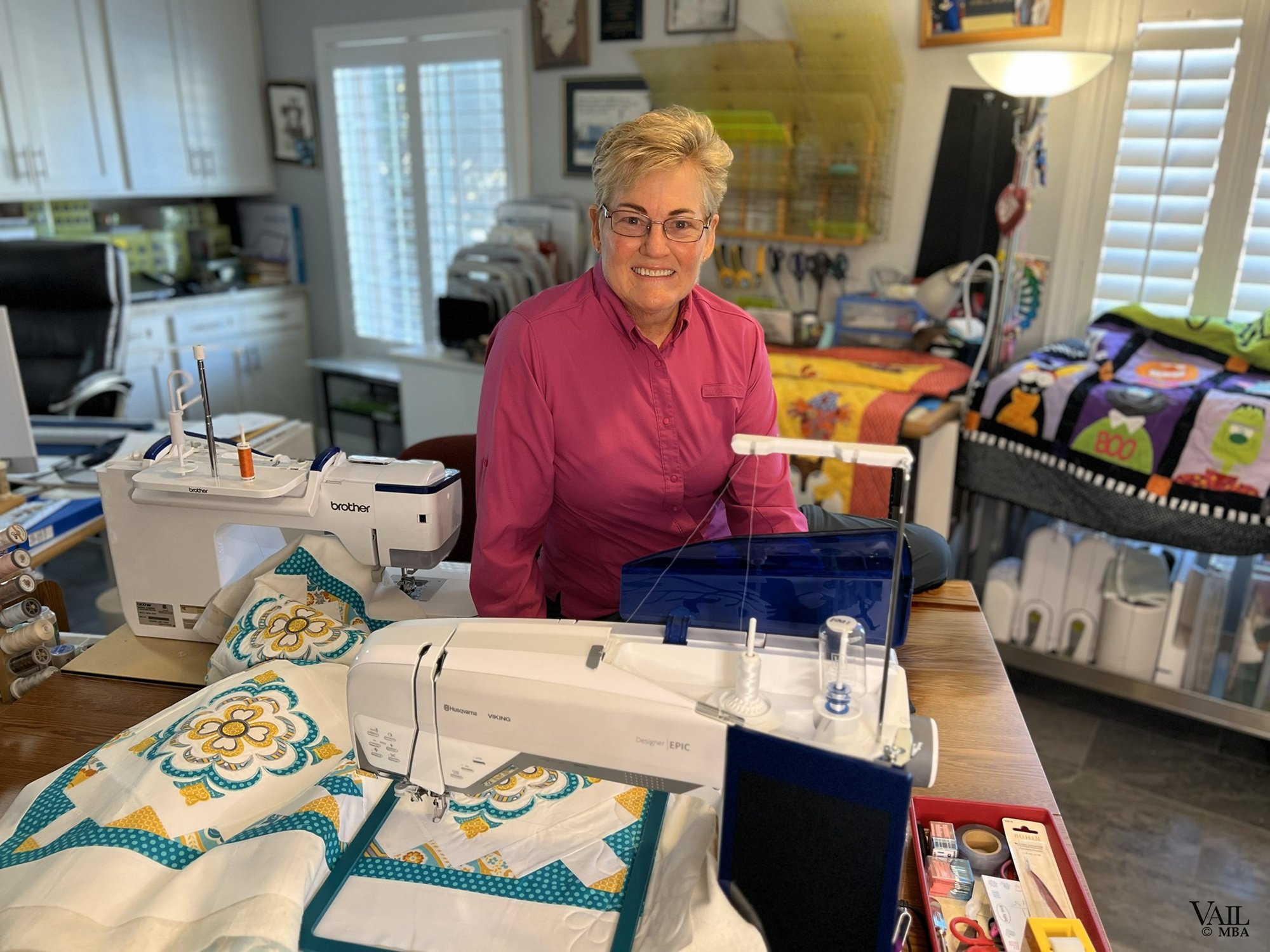 Professional photo of women in her sewing room with a collection of quilts displayed.