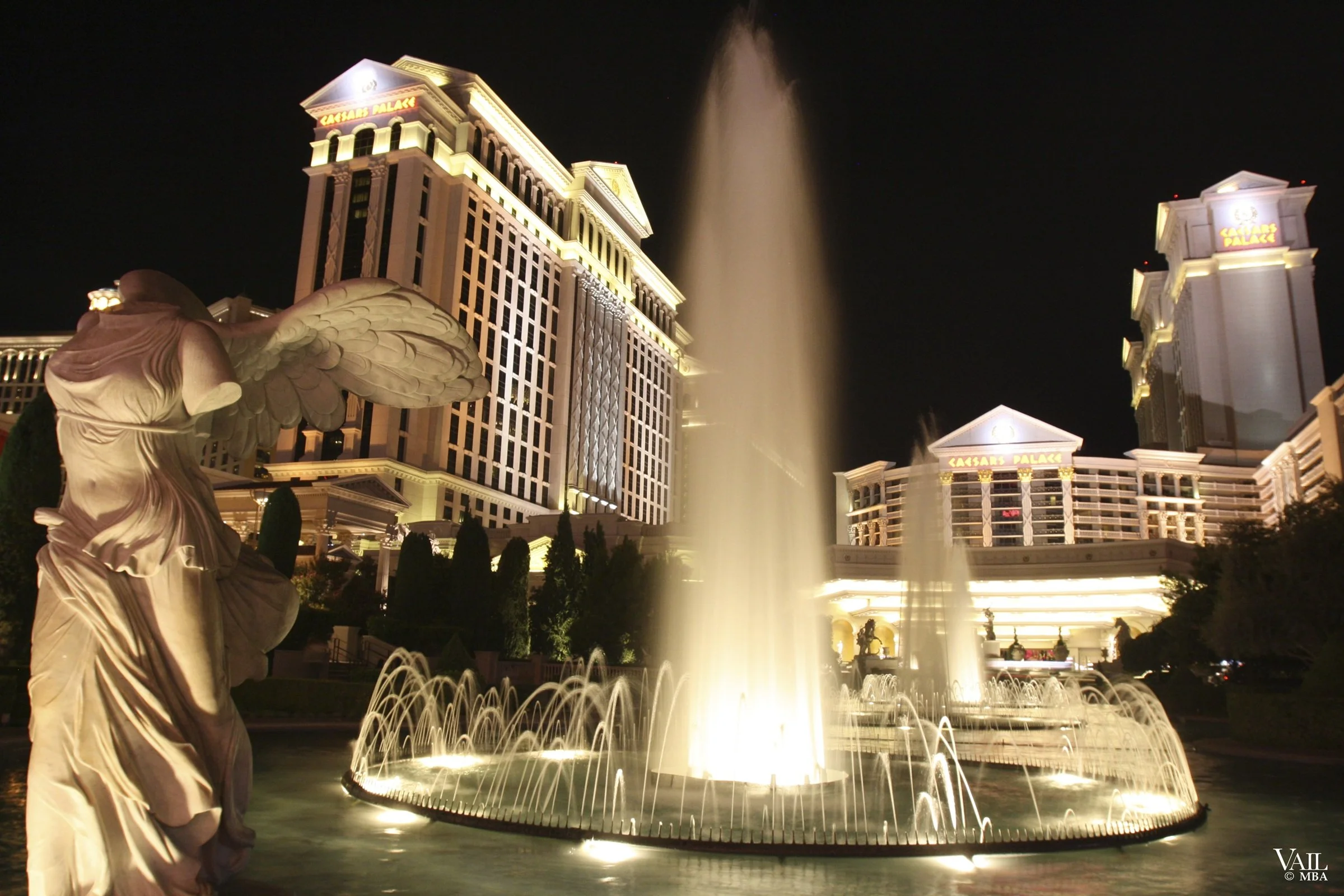 Night photo image shows the illuminated Caesars Palace hotel and casino in Las Vegas, with fountain.