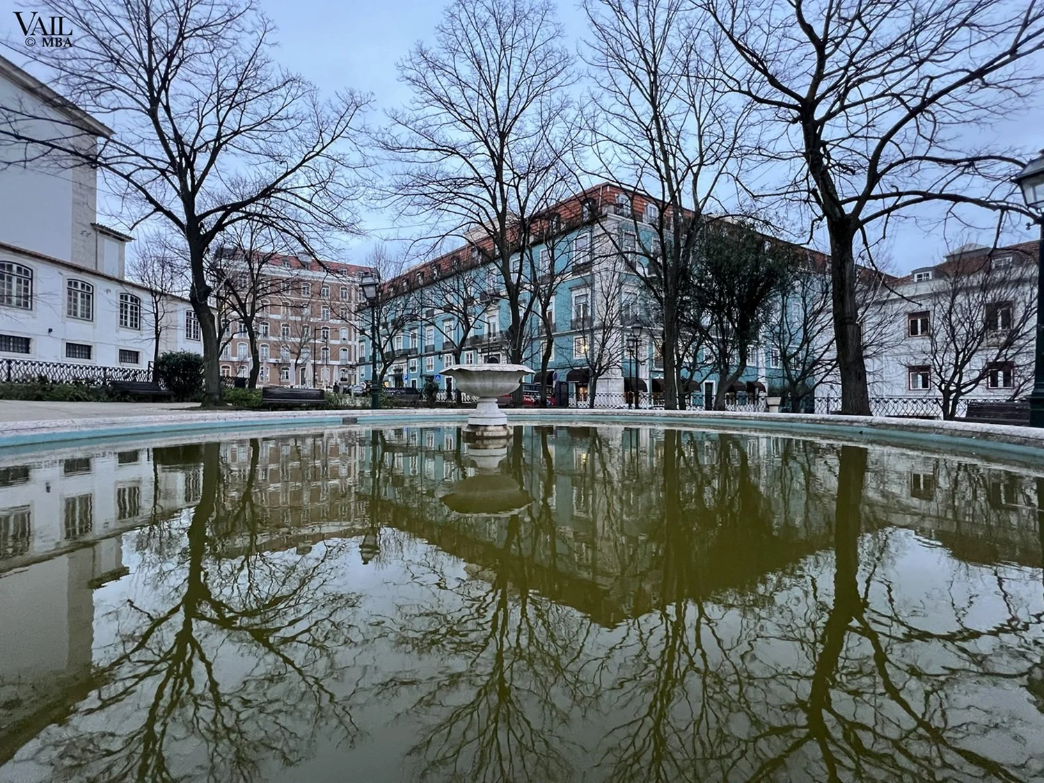 A fountain reflecting leafless trees and colored buildings, Lisbon, Portugal.