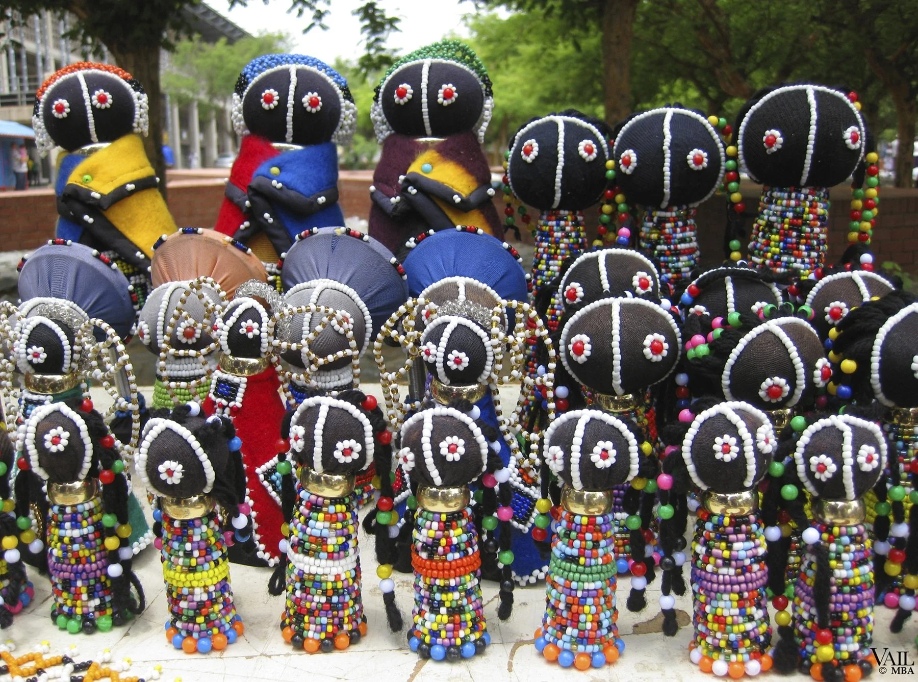 Display of colorful handmade beaded dolls with black faces, red and white flower designs, wearing vibrant clothes and jewelry, Cape Town South Africa.