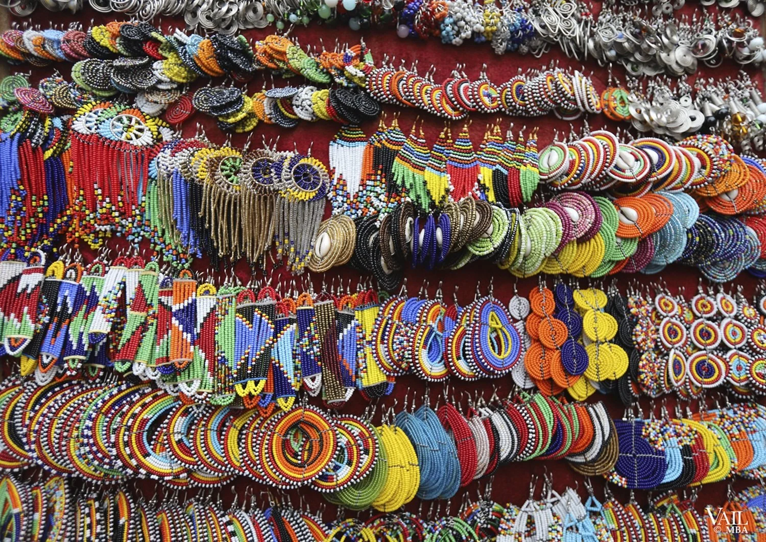 Colorful beaded necklaces and earrings displayed on a red fabric background at a Kenya market.
