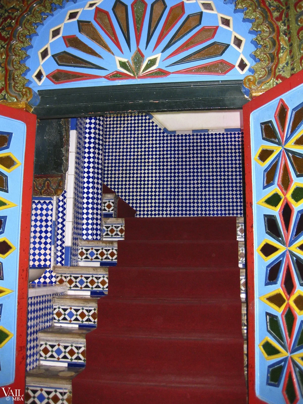 Colorful Moroccan entryway with blue, red, black, yellow, and green decorative tiles on the walls and archway, featuring geometric patterns and vibrant colors.