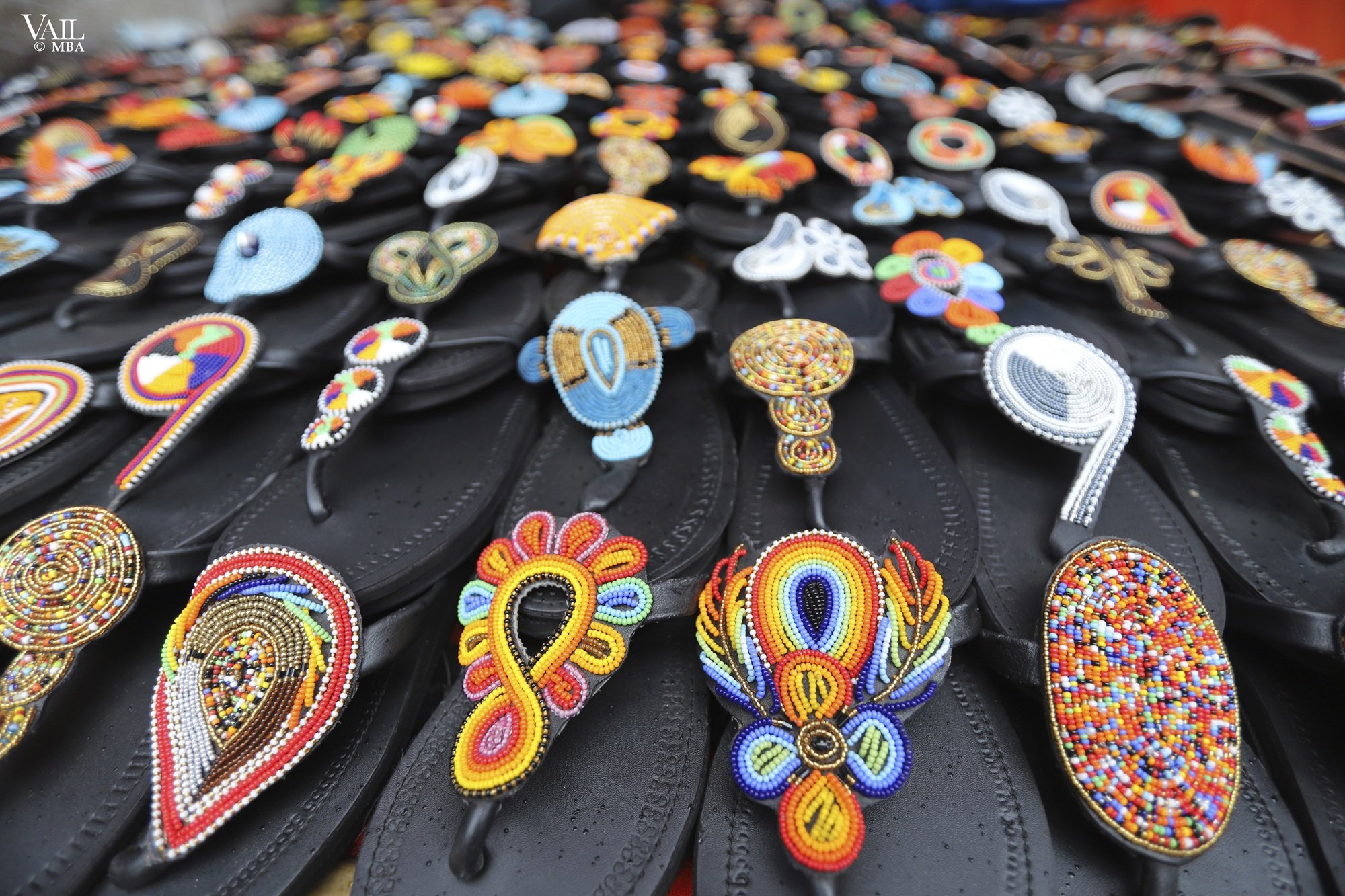 Display of various beaded embroidered sandal accessories on black sandals at an outdoor market in Kenya.