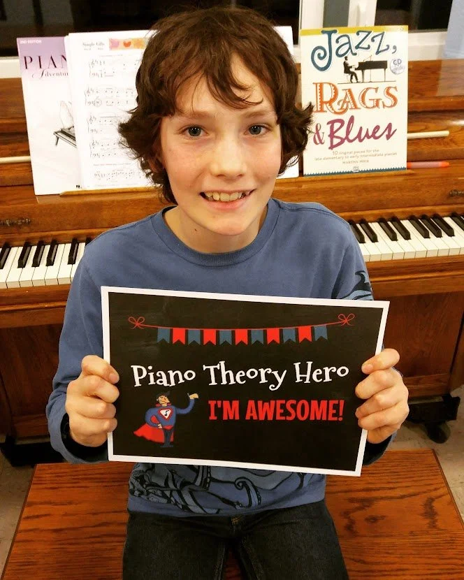 Smiling boy holds Piano Theory Hero sign