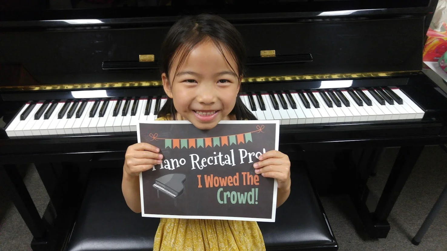 Smiling girl at piano holding sign “Piano Recital Pro”