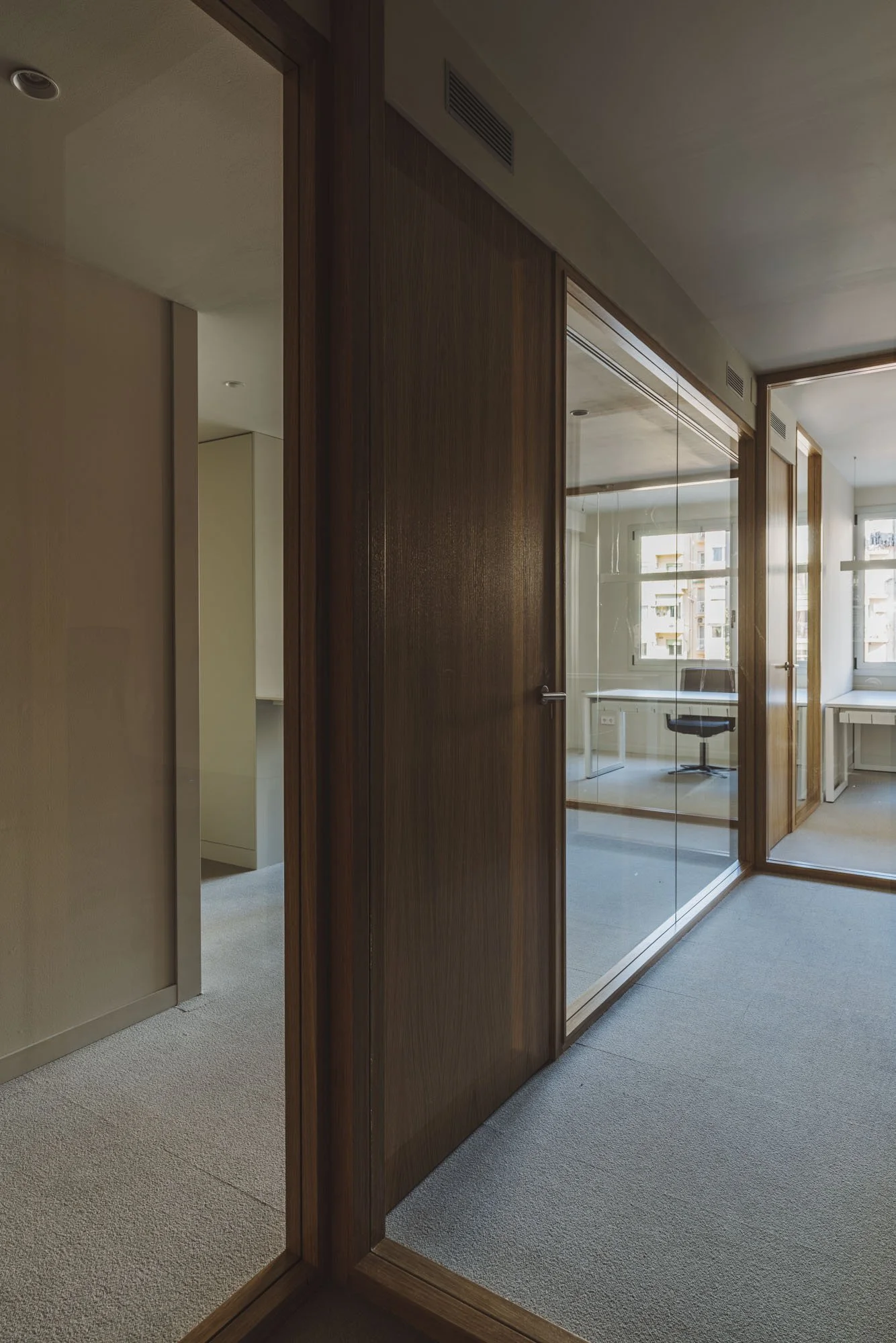 Espacio de oficina con paredes de madera, ventanas grandes y una sala de reuniones visible a través de un acristalado.